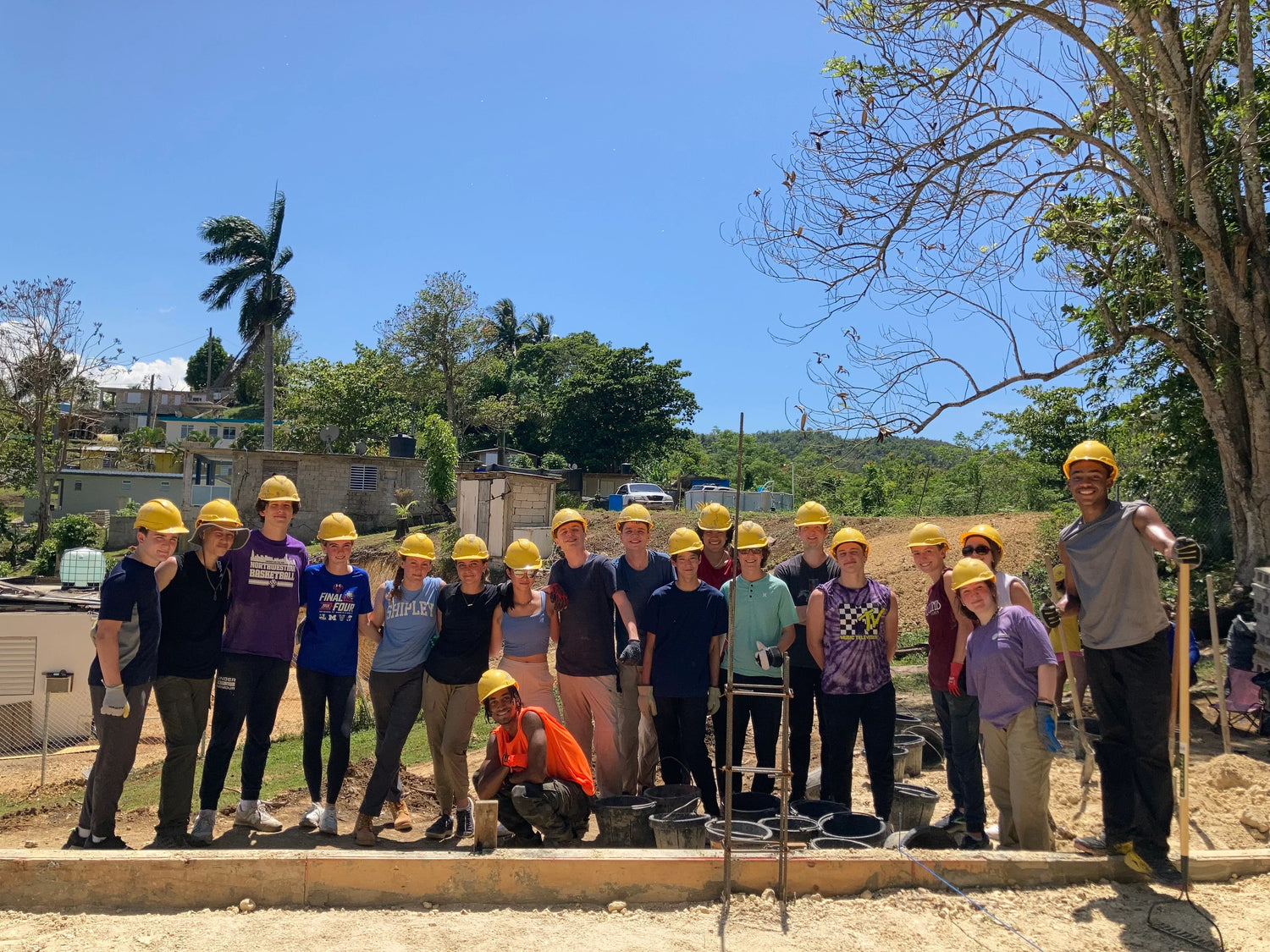 Group of teenagers in hard hats participating in a summer community service project outdoors.