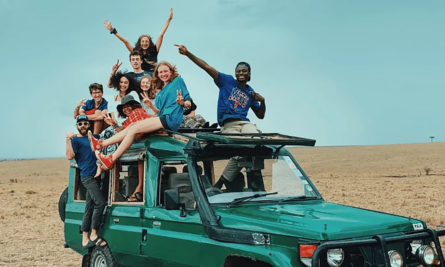 Group of high school students enjoying a summer gap program adventure on a jeep in a vast outdoor landscape.