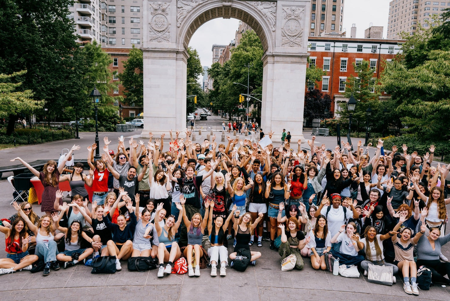 A large diverse group of middle and high school students celebrating together in front of an archway in a park.