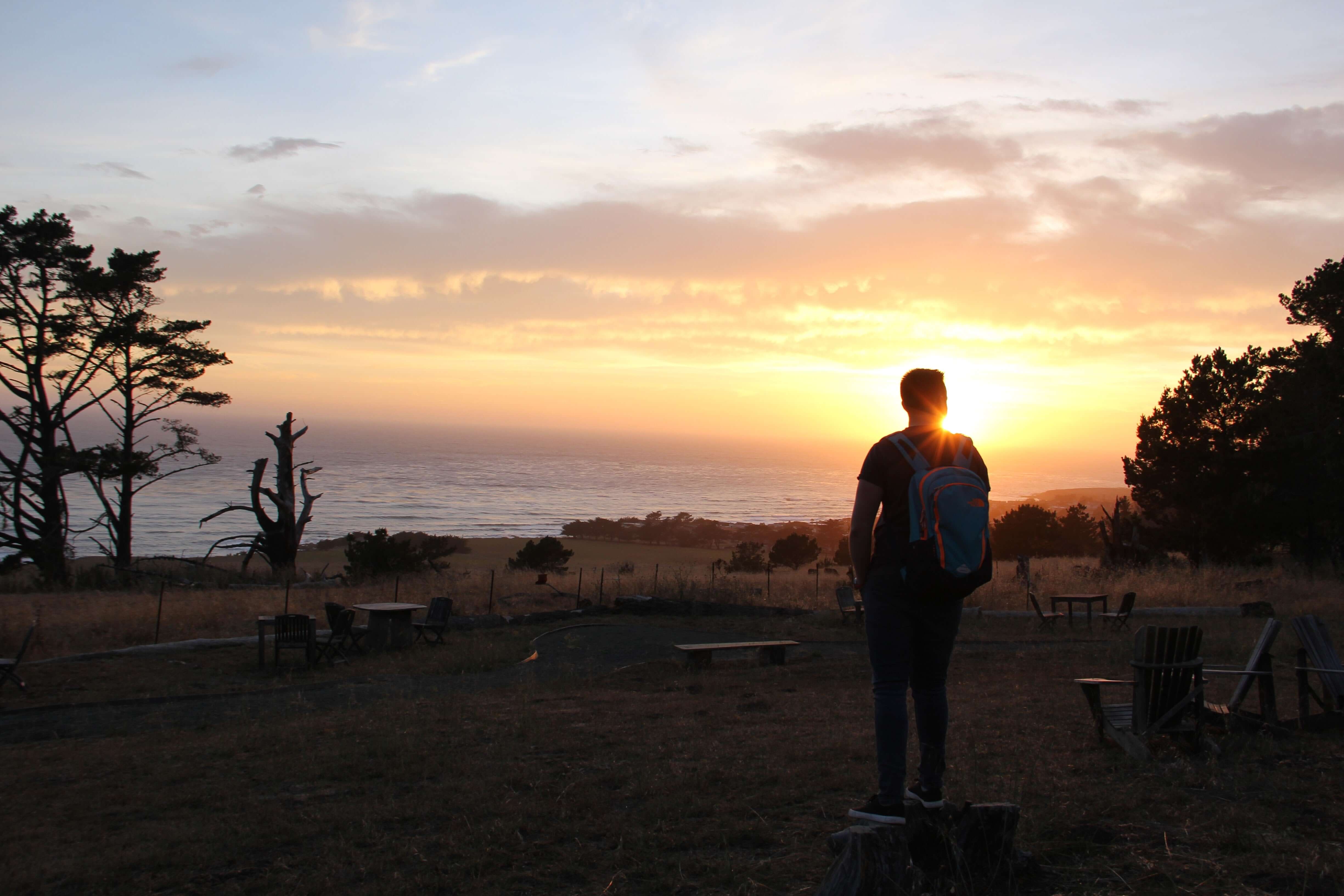A camper enjoying a sunset view over the ocean at Camp Ocean Pines, California, surrounded by nature's beauty.