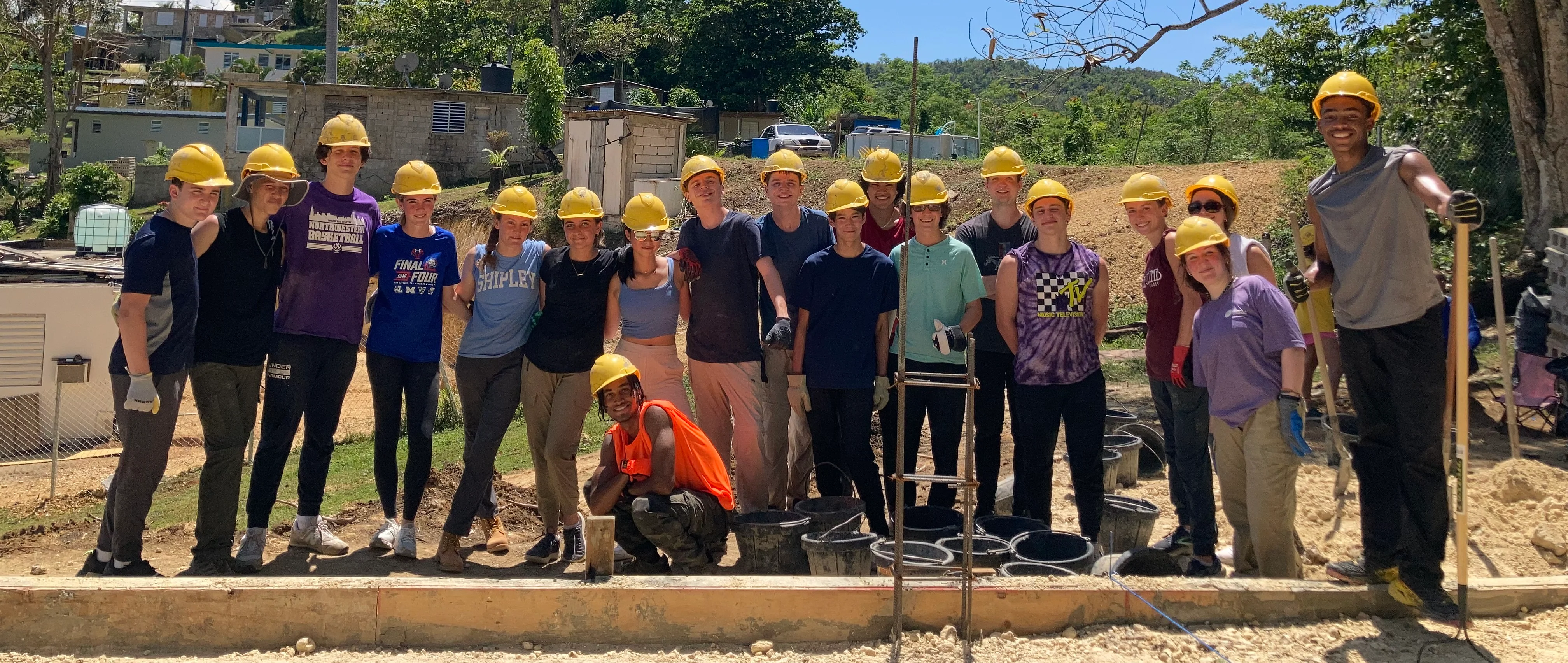 Group of volunteers in yellow hard hats working on a construction site, promoting teamwork and community service.