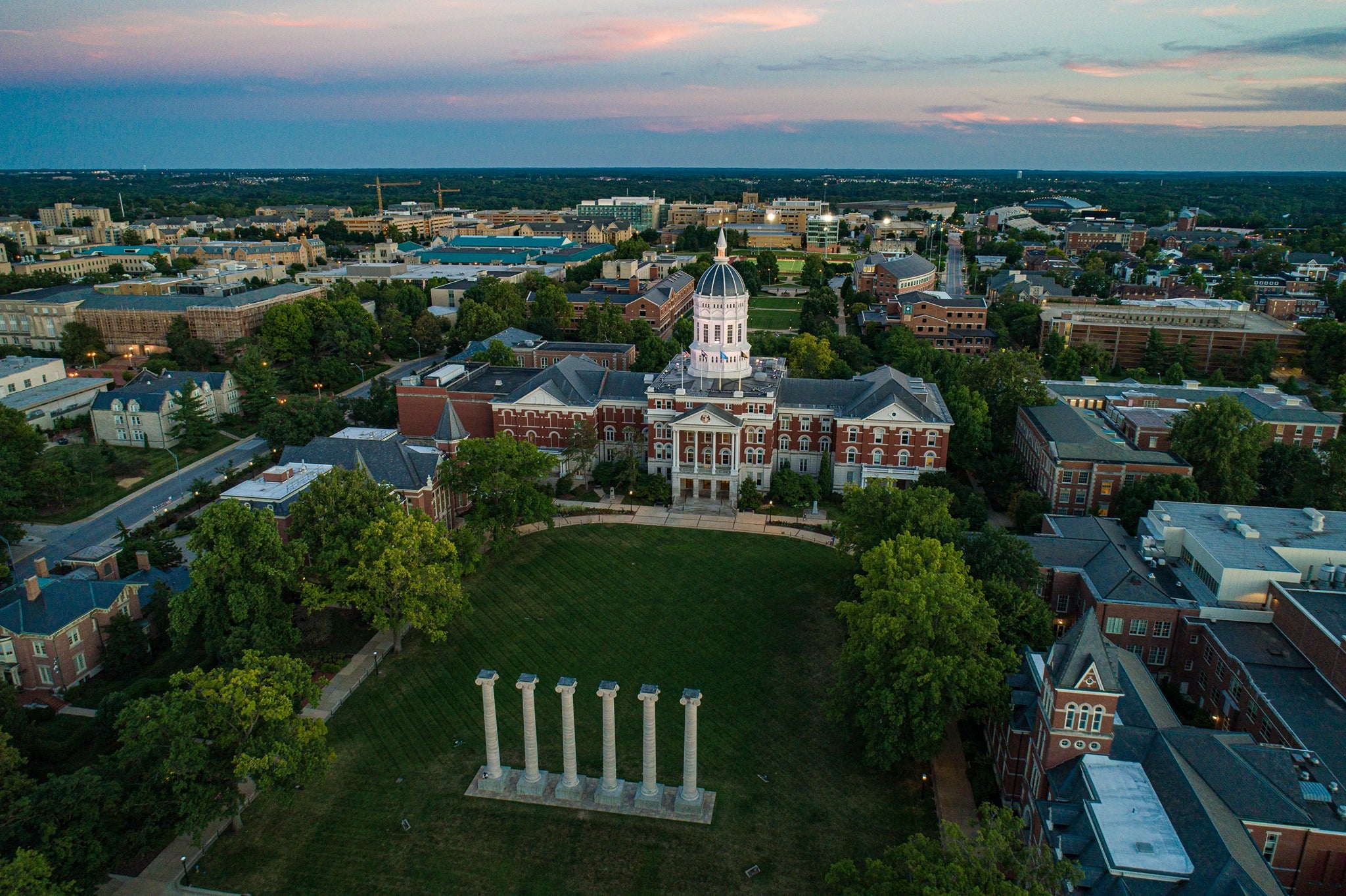 Aerial view of a college campus at sunset, featuring historic buildings and a prominent column structure.