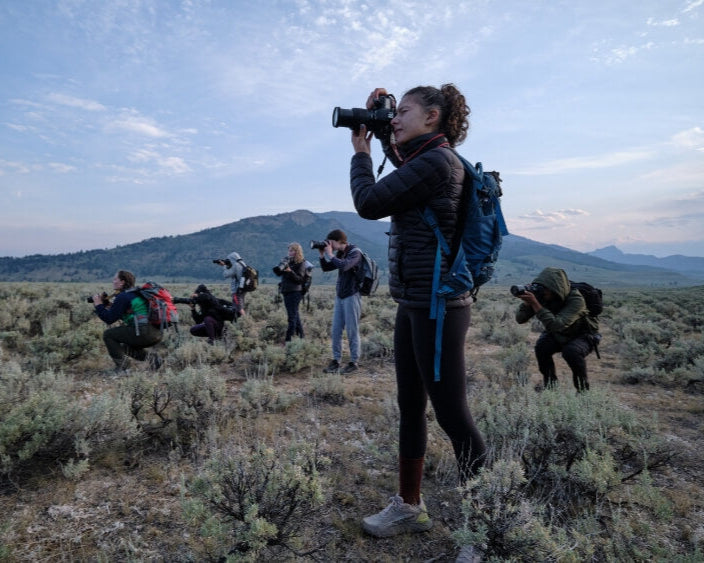 Students participating in a summer program photography workshop in a scenic outdoor landscape.