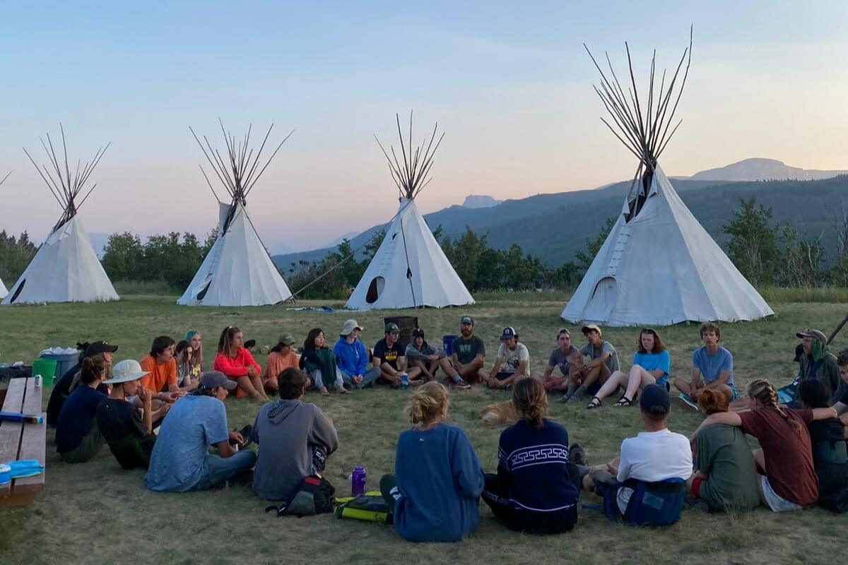 Group gathering around tipis during a summer program in Peru and Montana, promoting teamwork and community engagement.