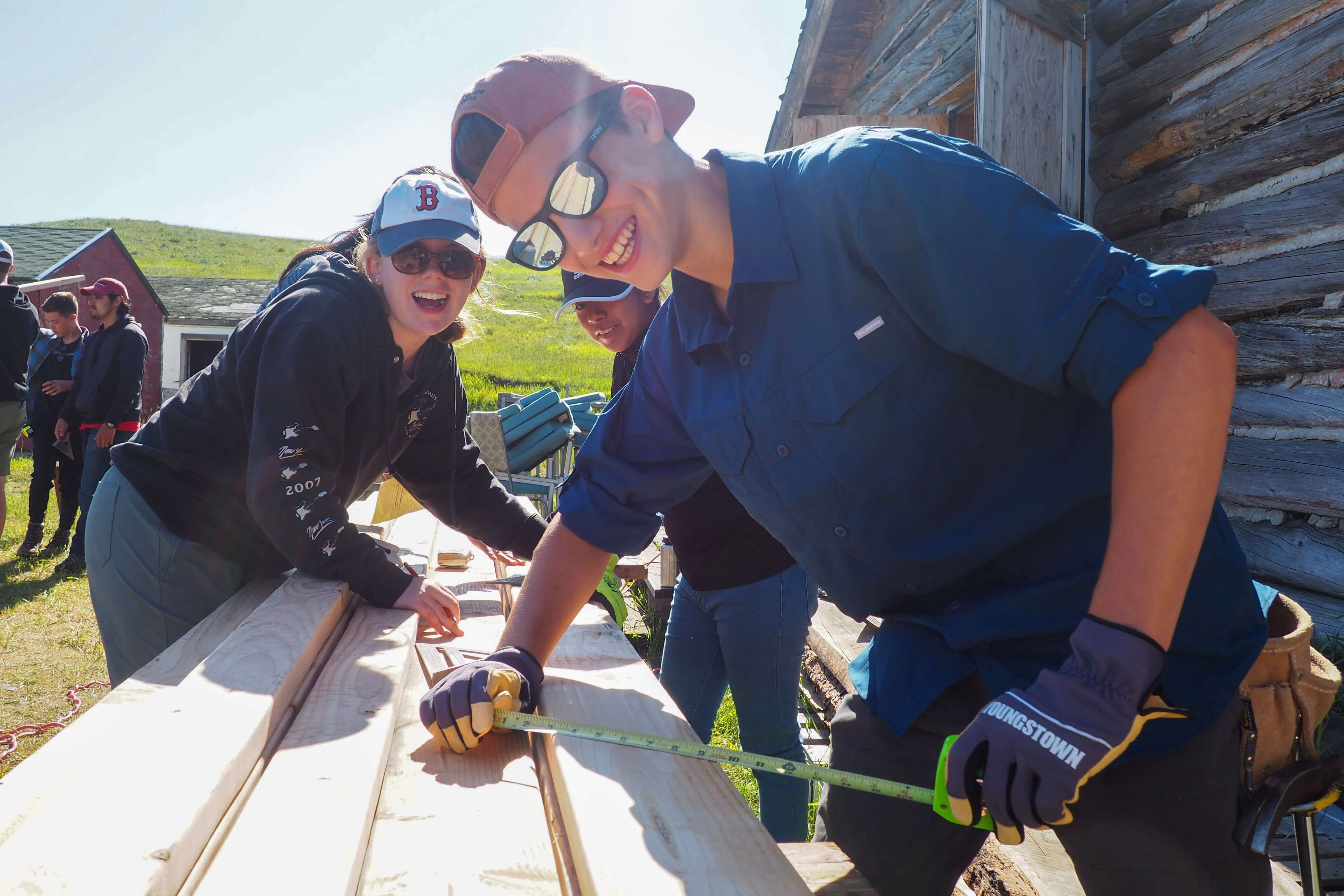 Summer program leaders in Peru, Montana, using tools for community service project, fostering teamwork and travel experiences.