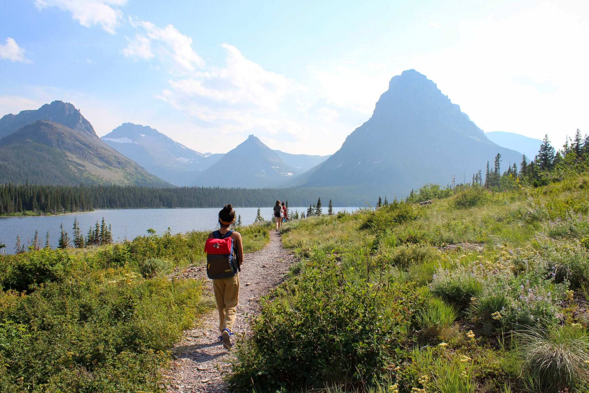 Person hiking on a scenic trail near a lake in the mountains, enjoying summer travel and nature.