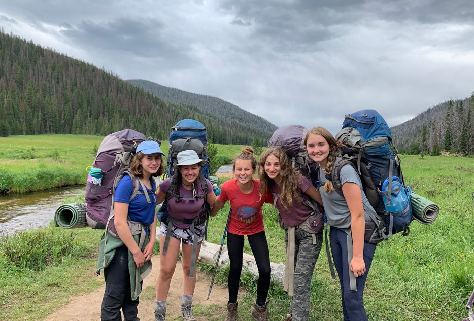 Five high school students with backpacks smiling during their Colorado summer camp adventure in nature.