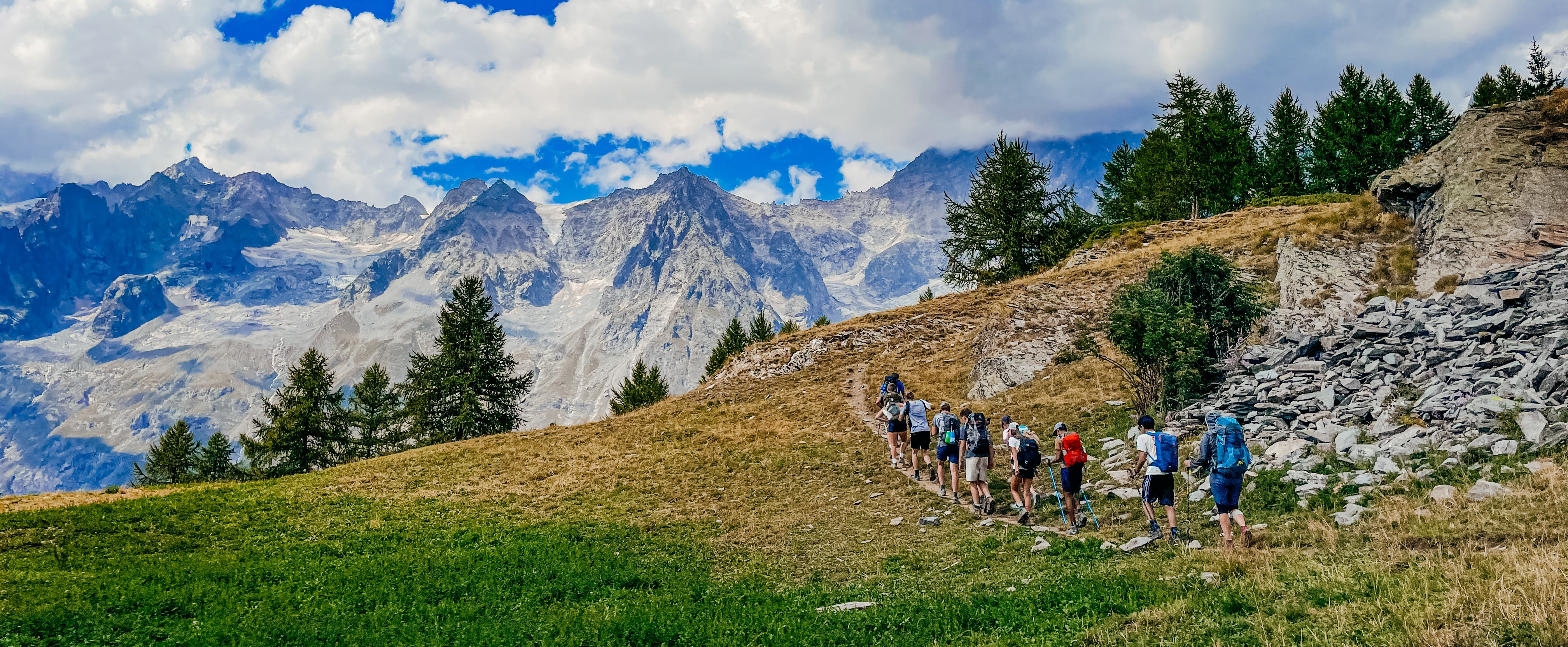 Group of hikers ascending a mountain trail in summer, surrounded by lush greenery and stunning mountain scenery.