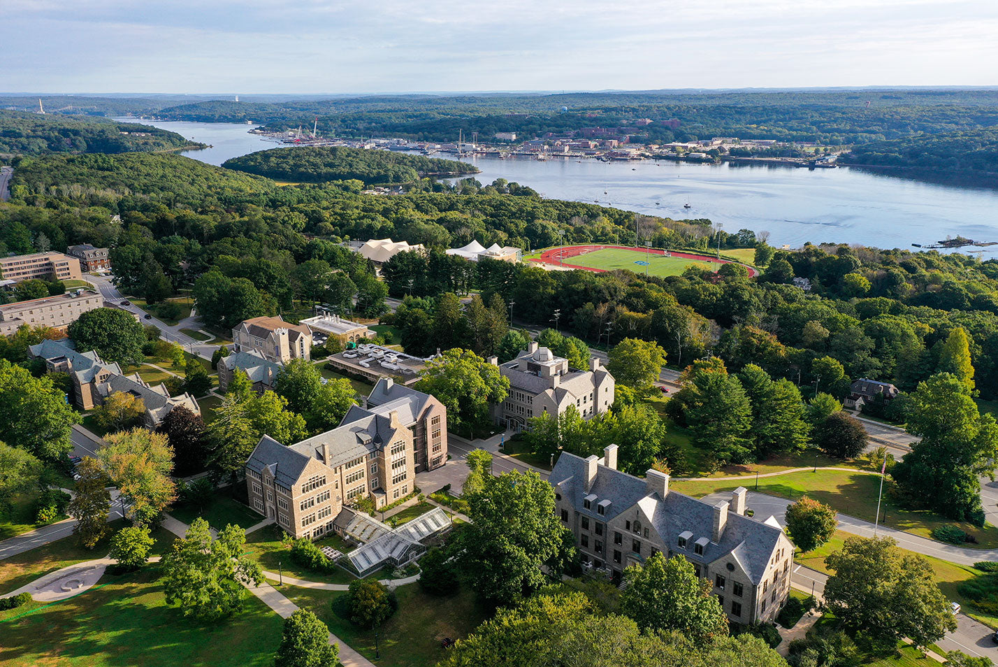 Aerial view of a college campus surrounded by lush greenery and a river, ideal for summer programs and high school camps.