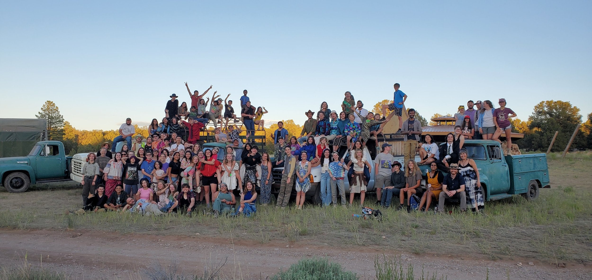 Group photo of students enjoying a summer camp program outdoors, surrounded by vintage trucks and a scenic landscape.