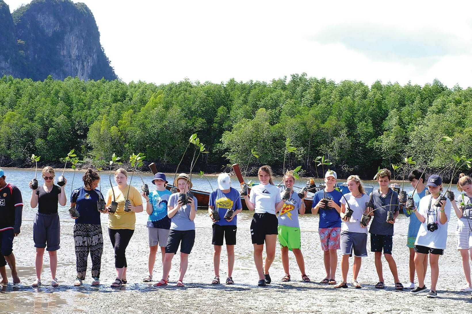 Group of students participating in marine conservation by planting mangroves in Thailand's coastal area.