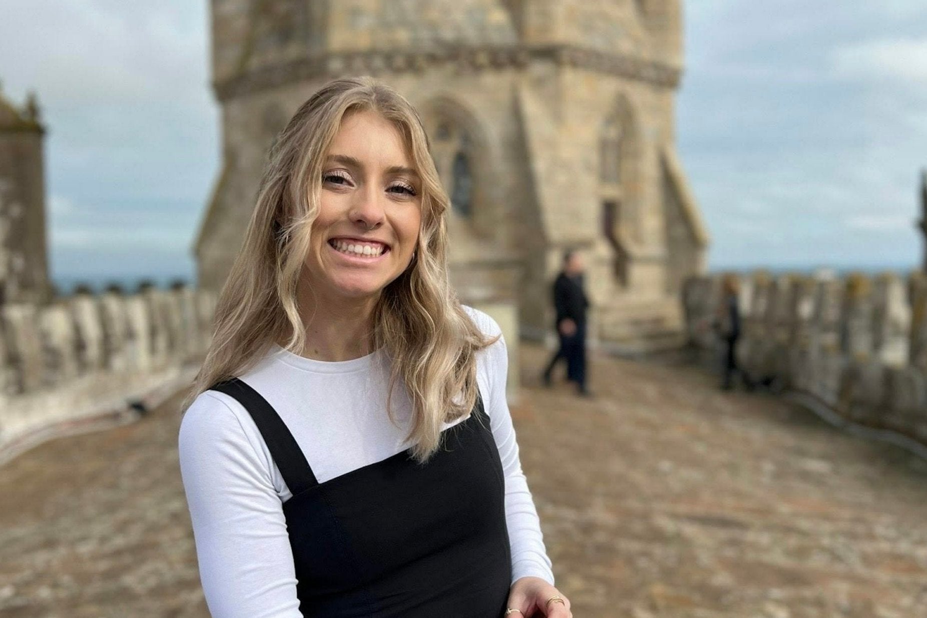 Young woman smiling at a historic tower, enjoying her summer travels in Portugal. Perfect for teen travel programs.
