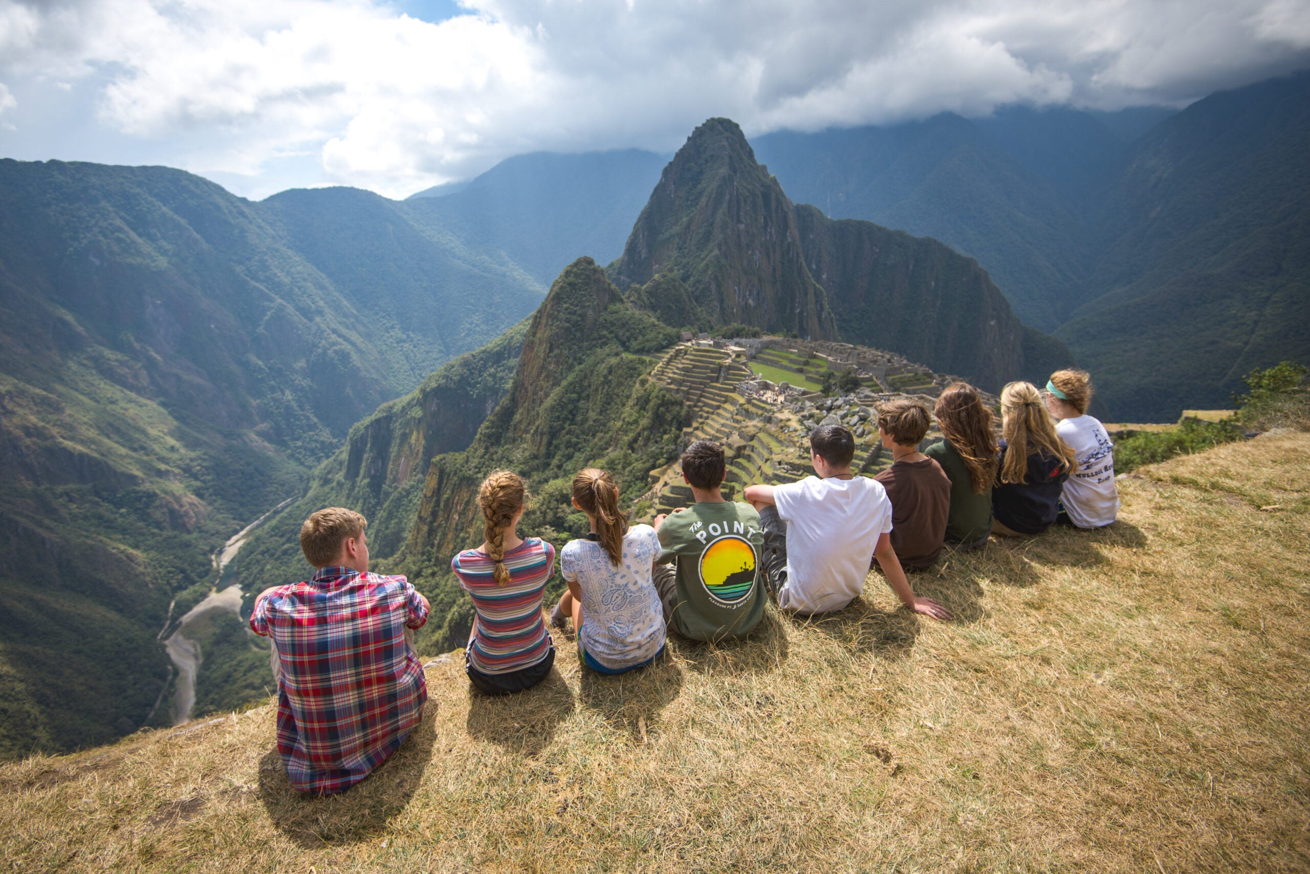 Group of young people overlooking Machu Picchu, enjoying a summer camp adventure amidst stunning mountain scenery.