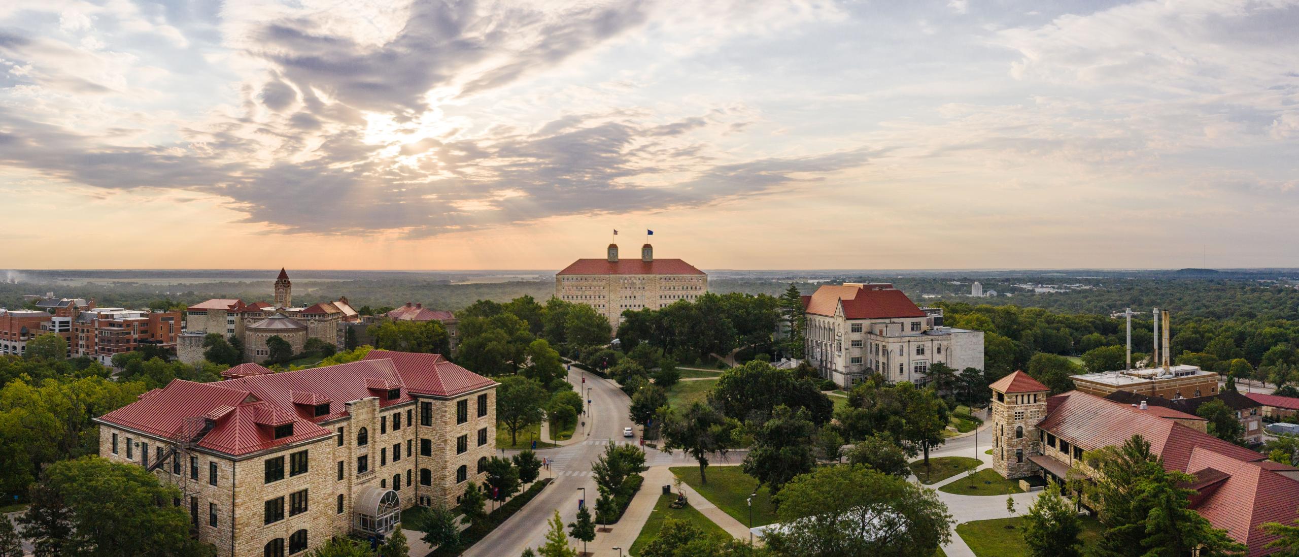 Aerial view of a college campus with red-roofed buildings and trees under a cloudy sunset sky, ideal for summer programs.