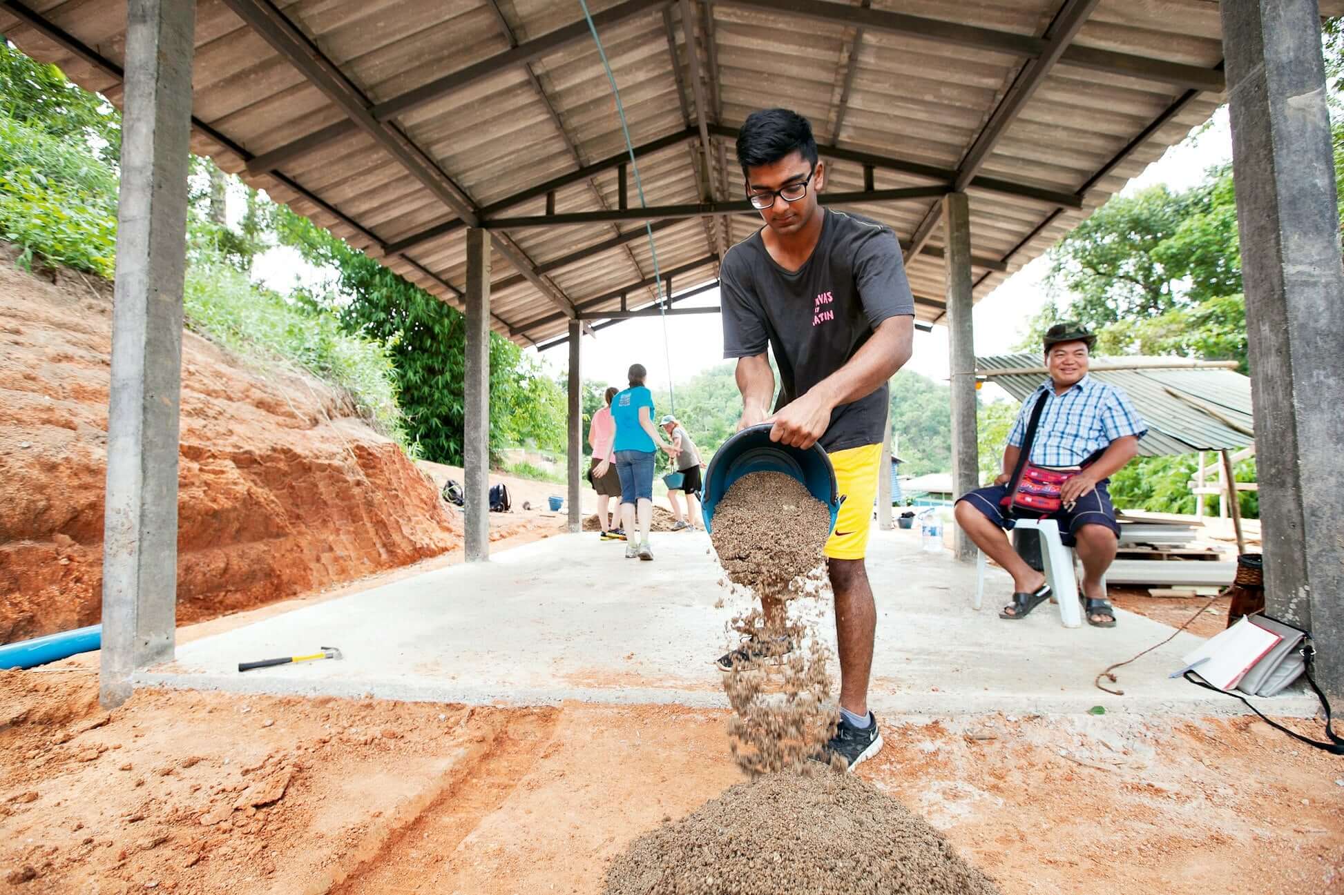 Teen participant pouring sand during a service expedition in remote Thailand, enhancing hands-on learning experience.