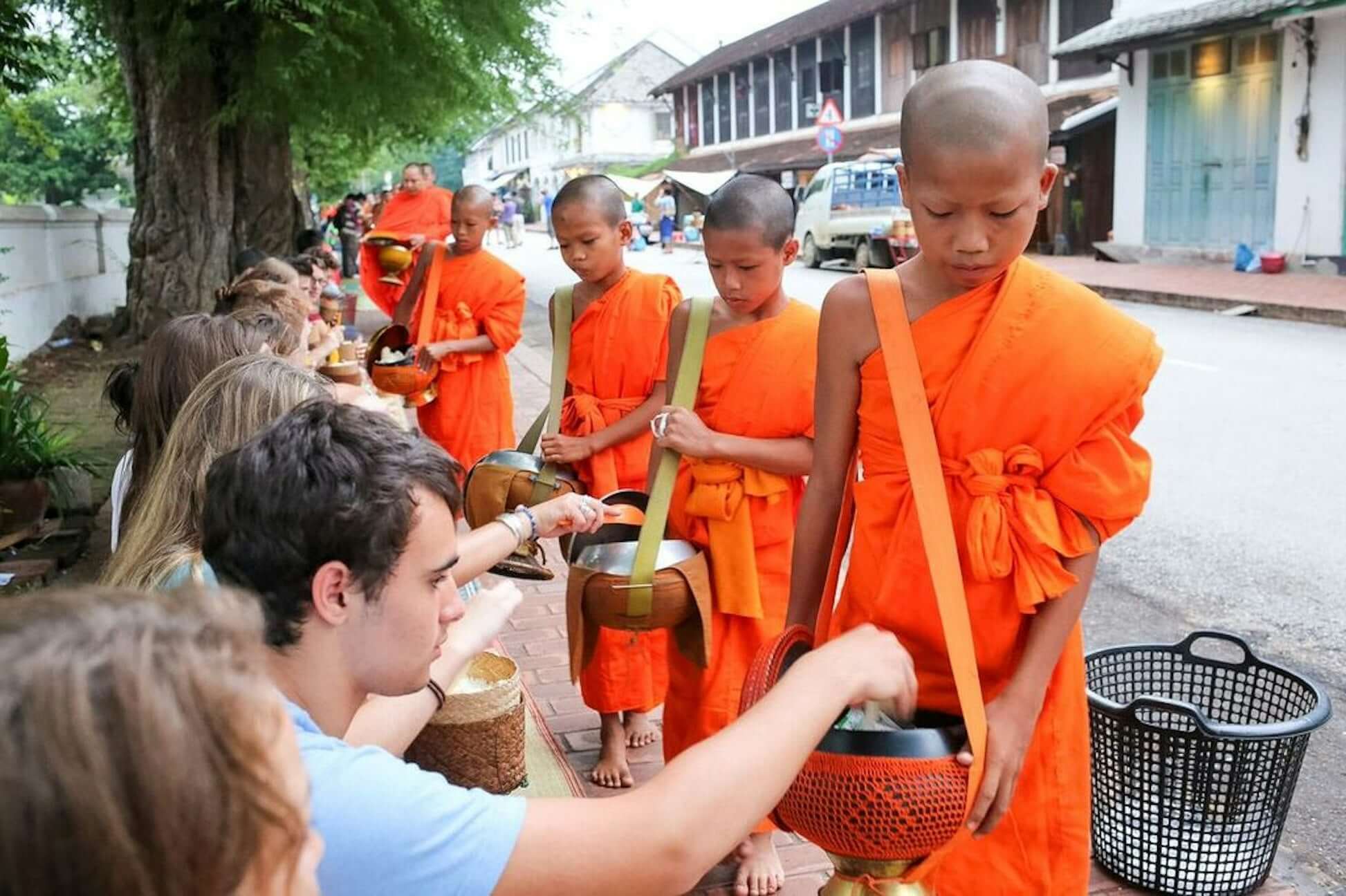 High school students participating in a traditional Buddhist almsgiving ceremony with young monks in Thailand.