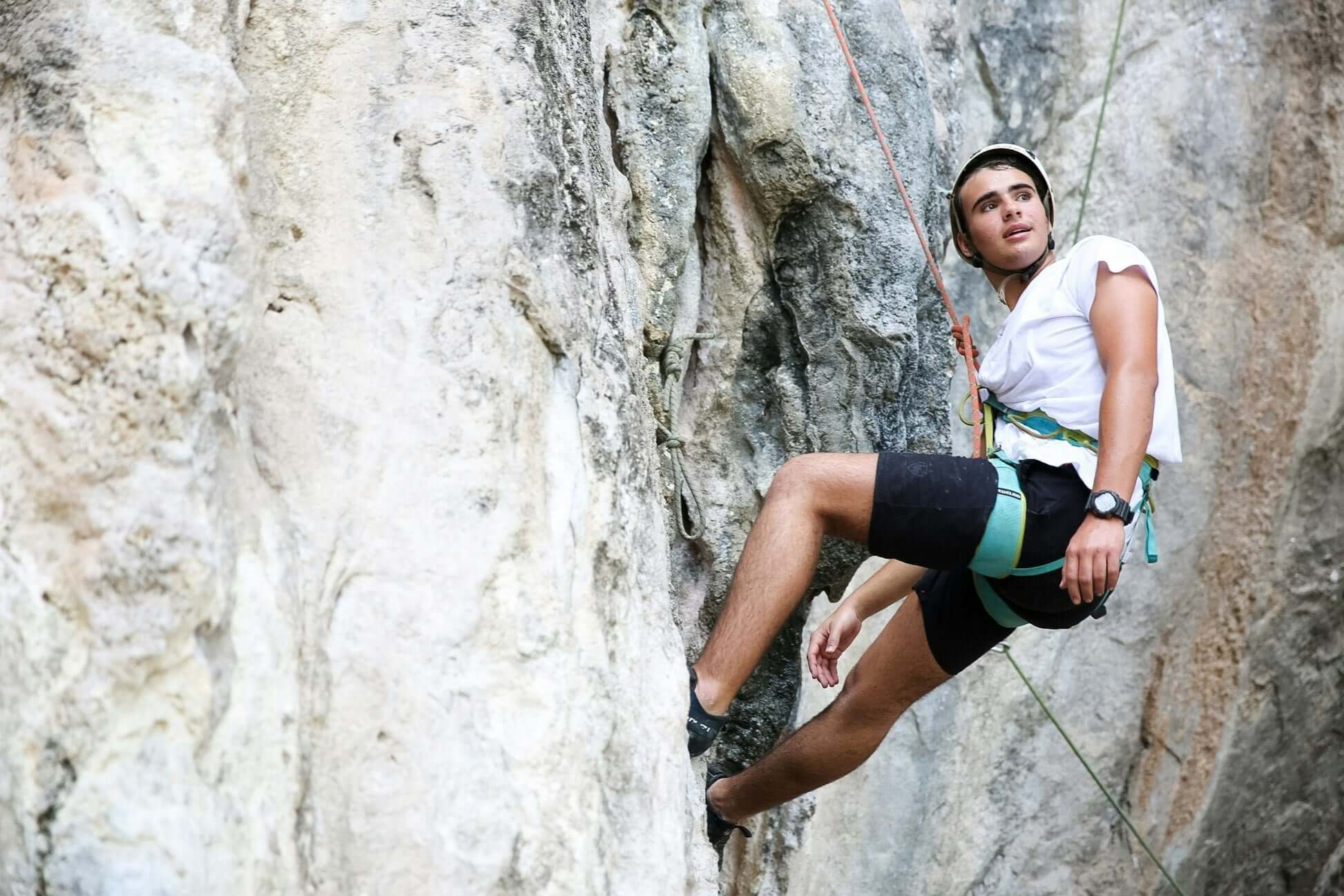 High school student rock climbing on a limestone cliff in Thailand during an adventurous travel experience.