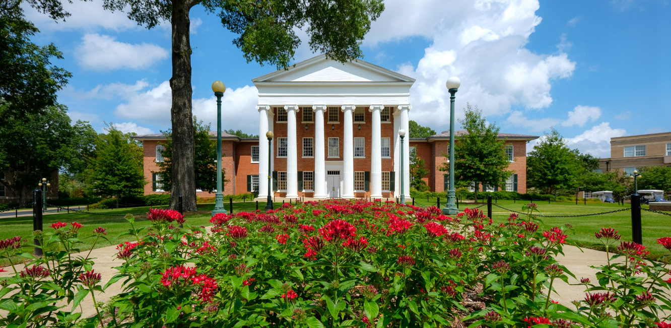 Summer programs at a college campus with blooming flowers and classic architecture under a blue sky.