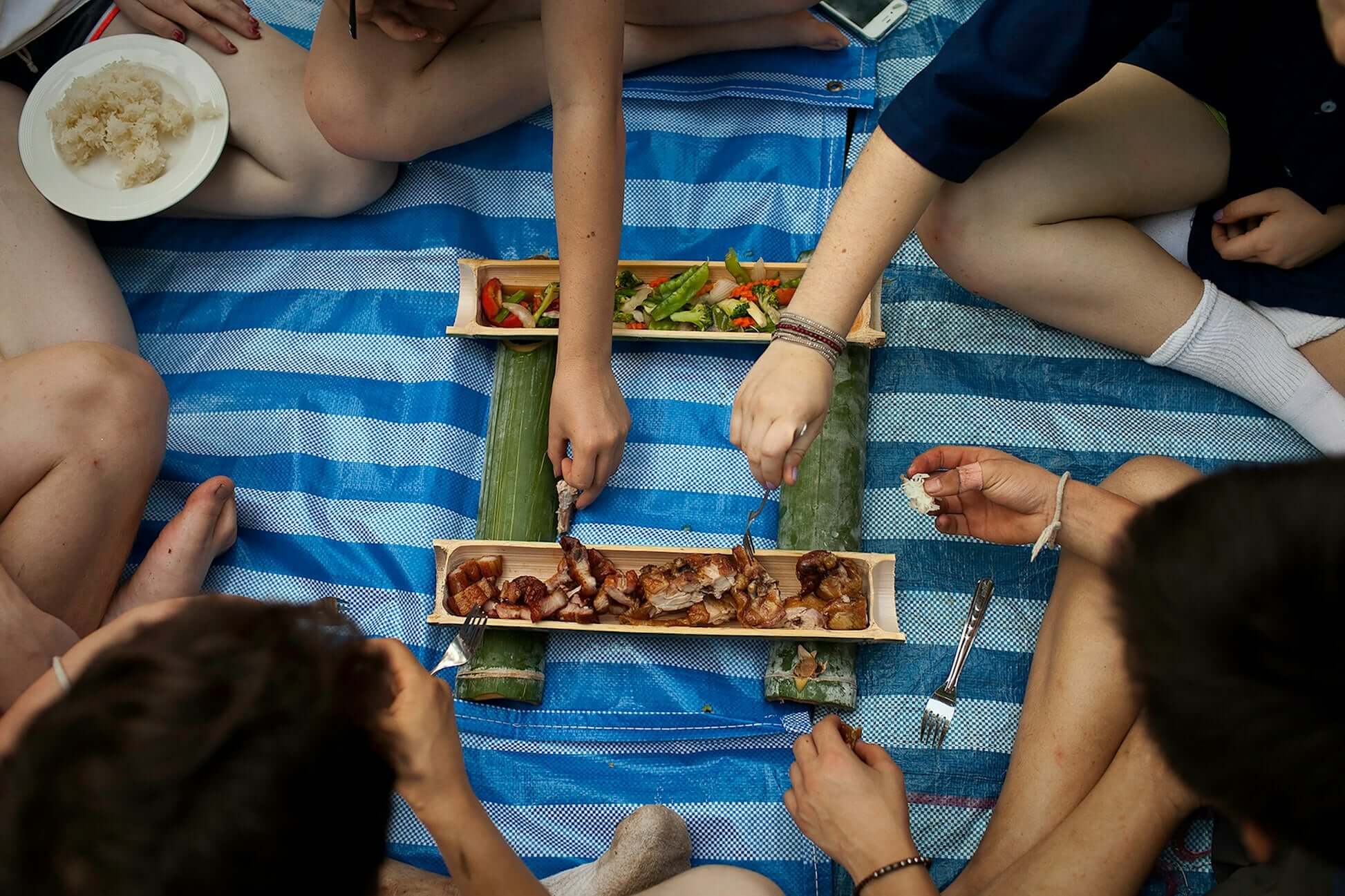 friends enjoying a delicious meal together outdoors on a blue blanket, sharing delicious food and laughter.