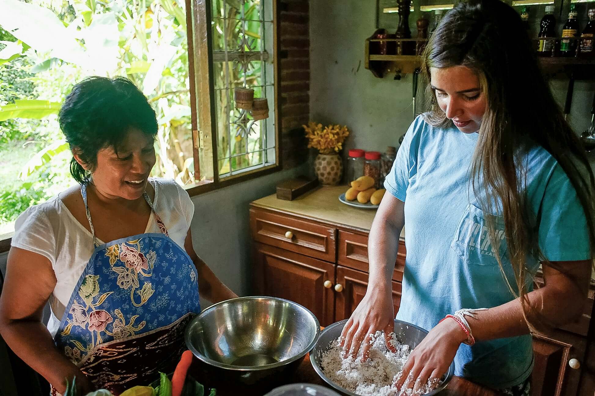Two women cooking together in a kitchen, learning traditional Thai cooking techniques during a cultural experience.