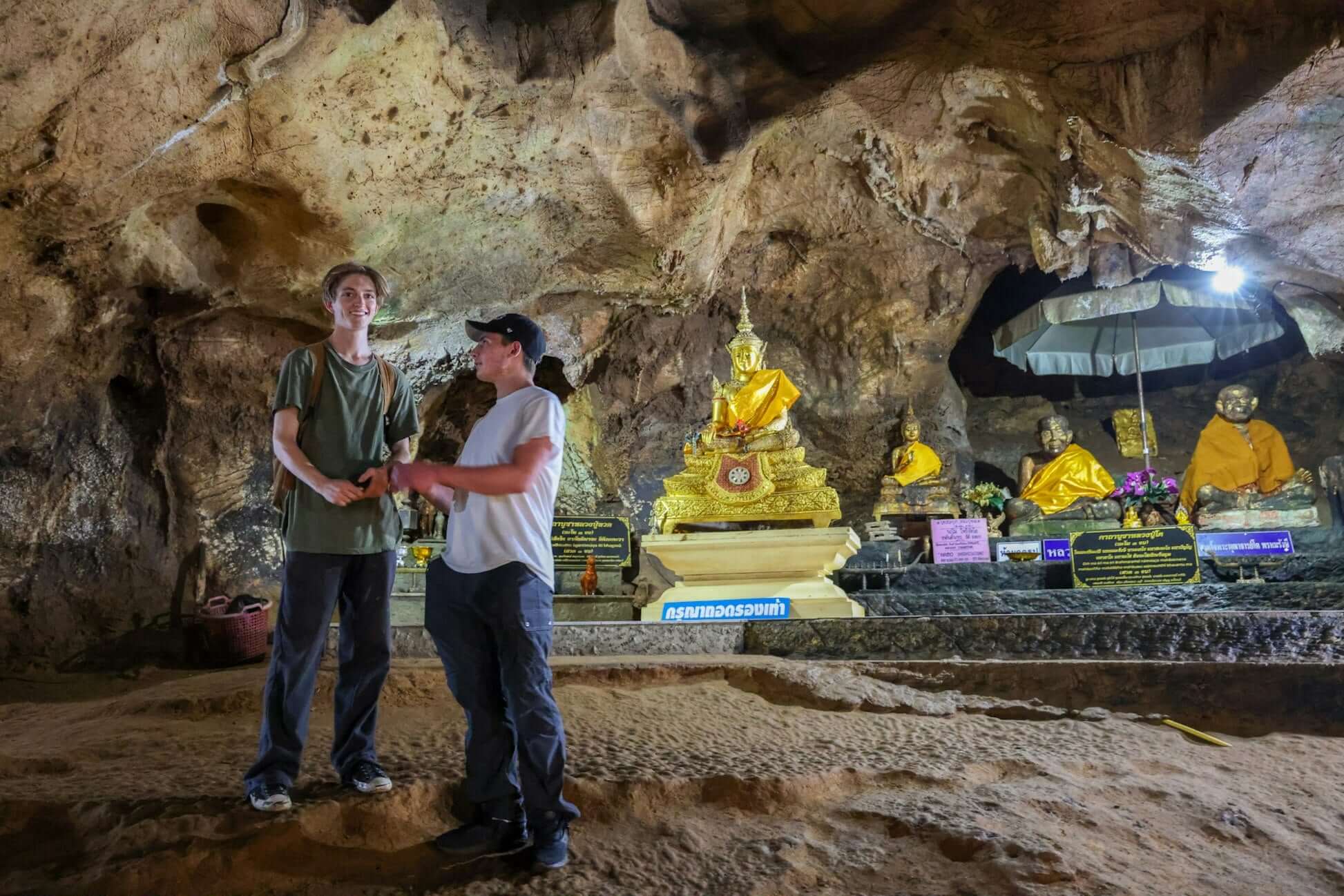 High school students exploring a cave with golden Buddha statues in northern Thailand's adventure travel experience.