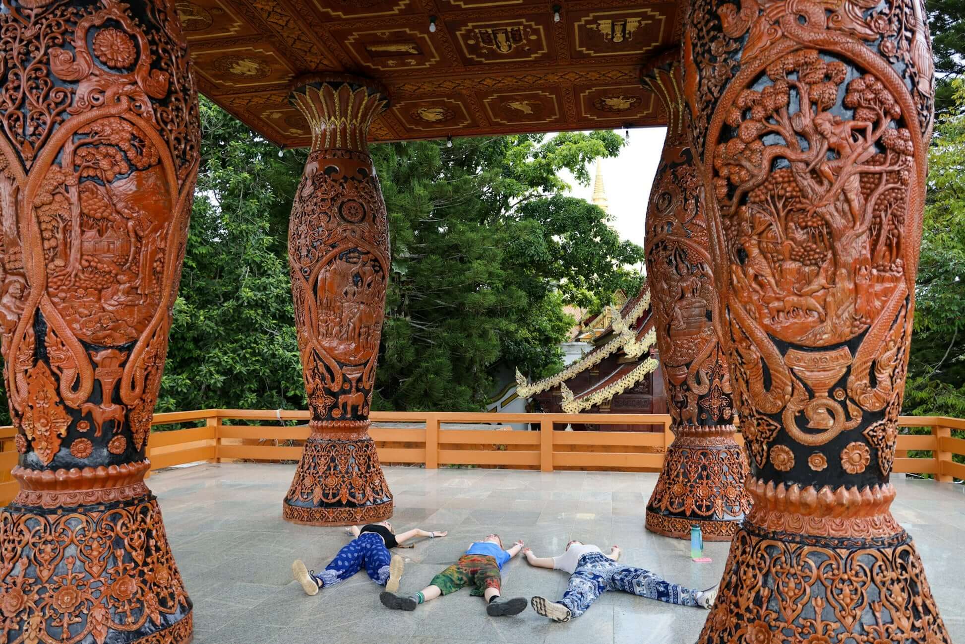 High school students relaxing under intricately carved pillars at a temple in northern Thailand's lush landscape.