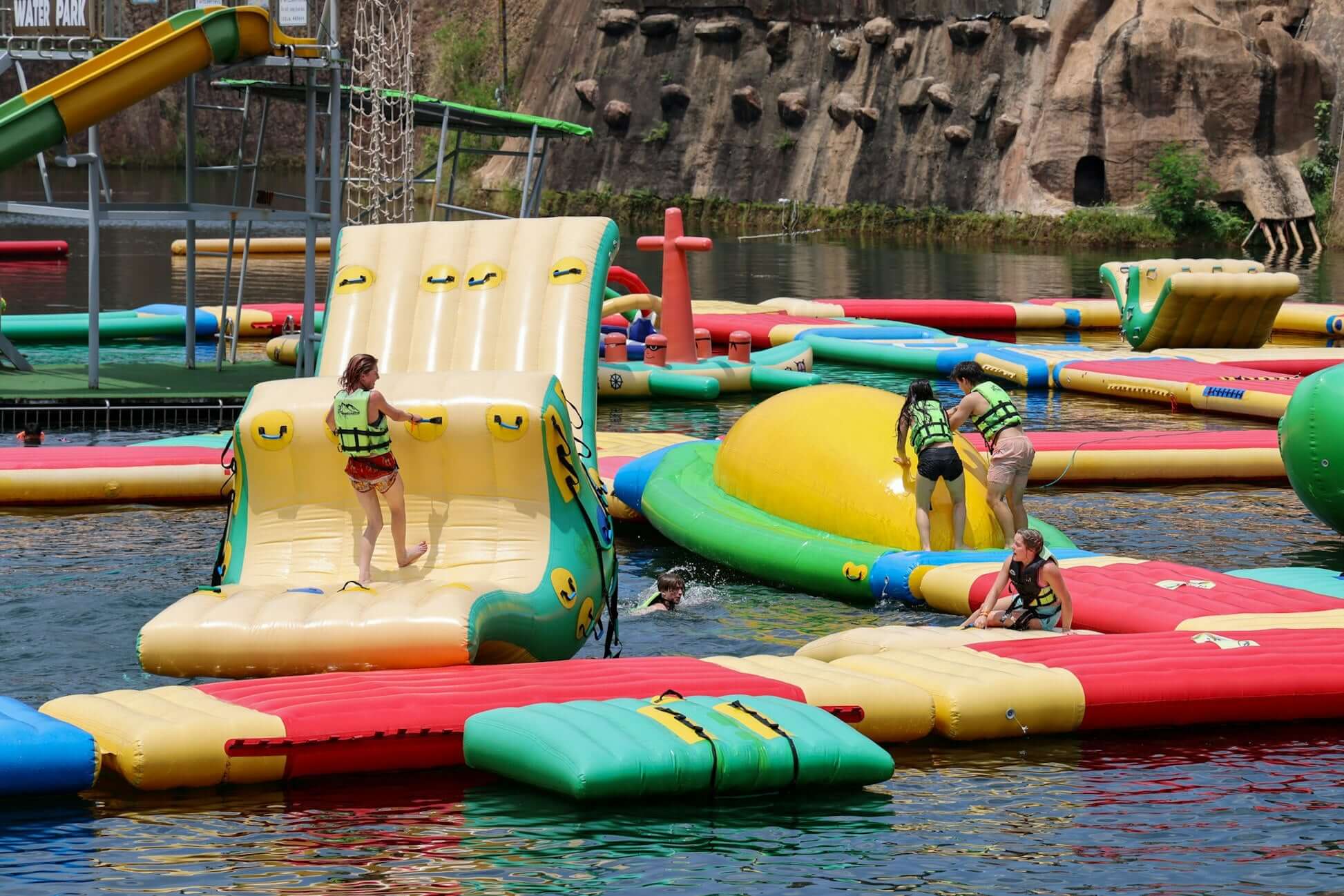 Kids in life jackets playing on colorful water inflatables at a summer water park. Perfect for teen summer activities.