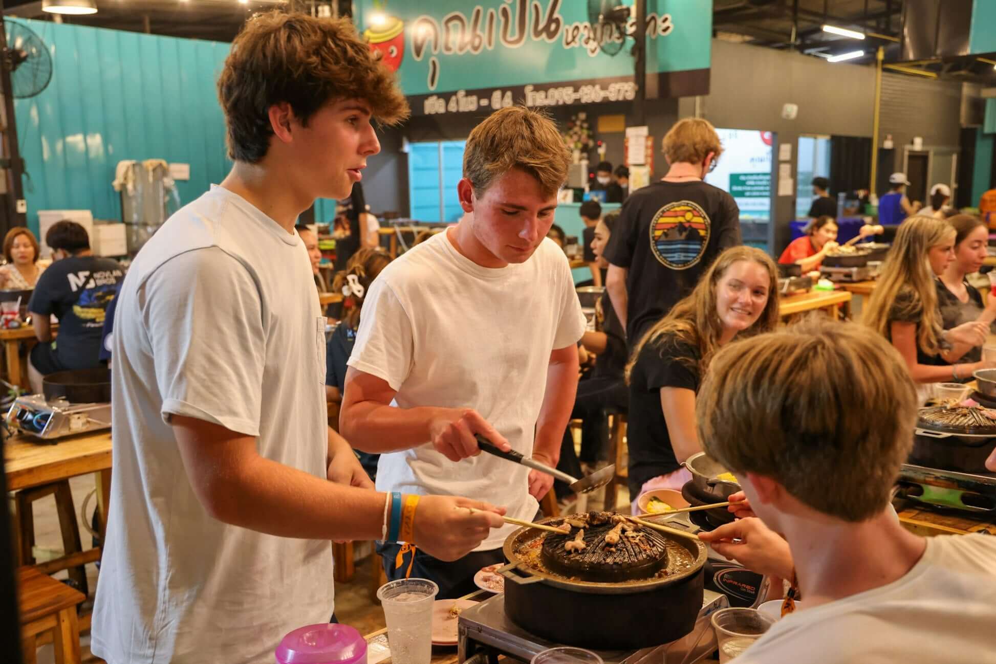 High school students enjoying a traditional Thai barbecue experience at a local restaurant in Thailand.