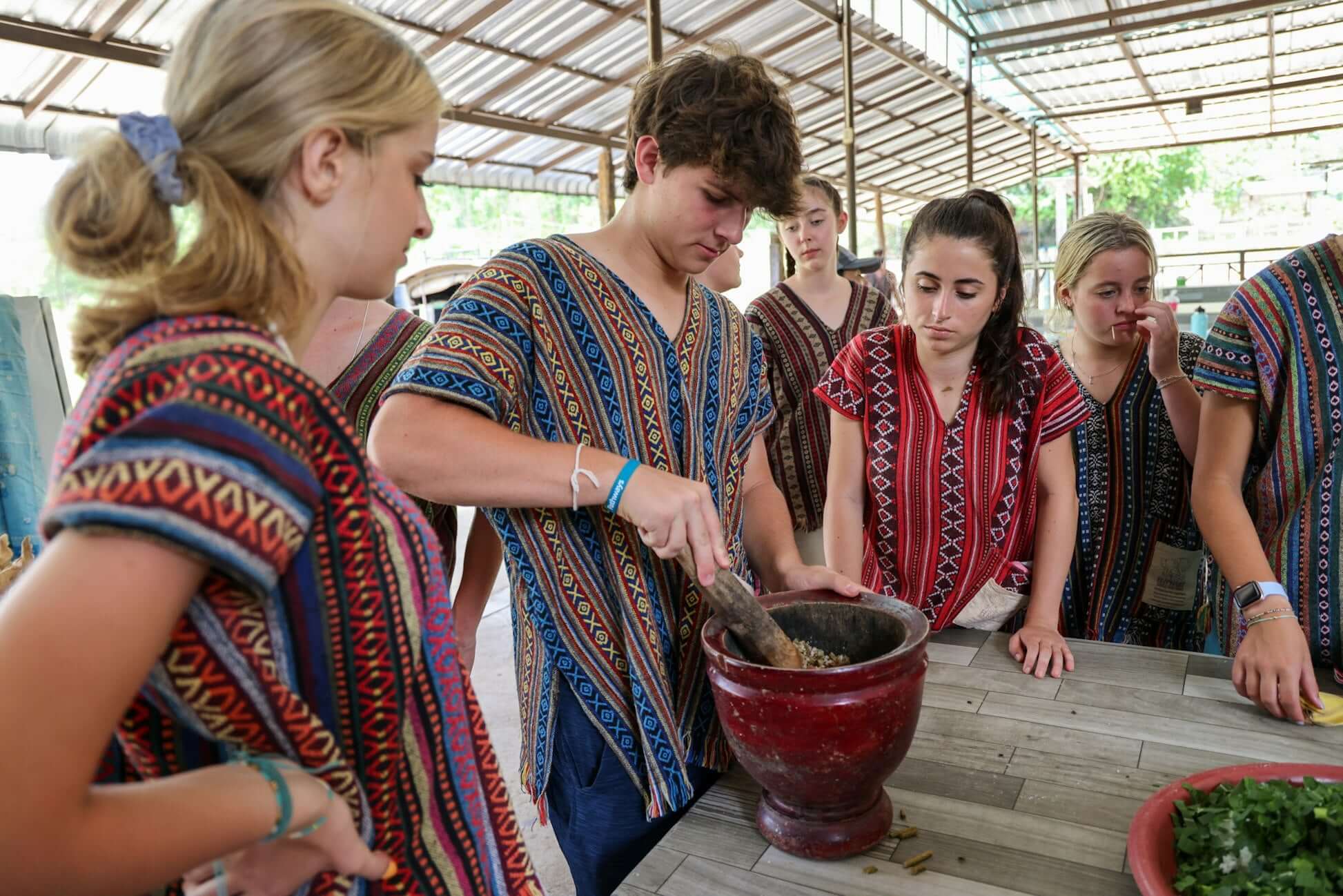 Teens in traditional attire learning to prepare food together during a cultural experience in Thailand.