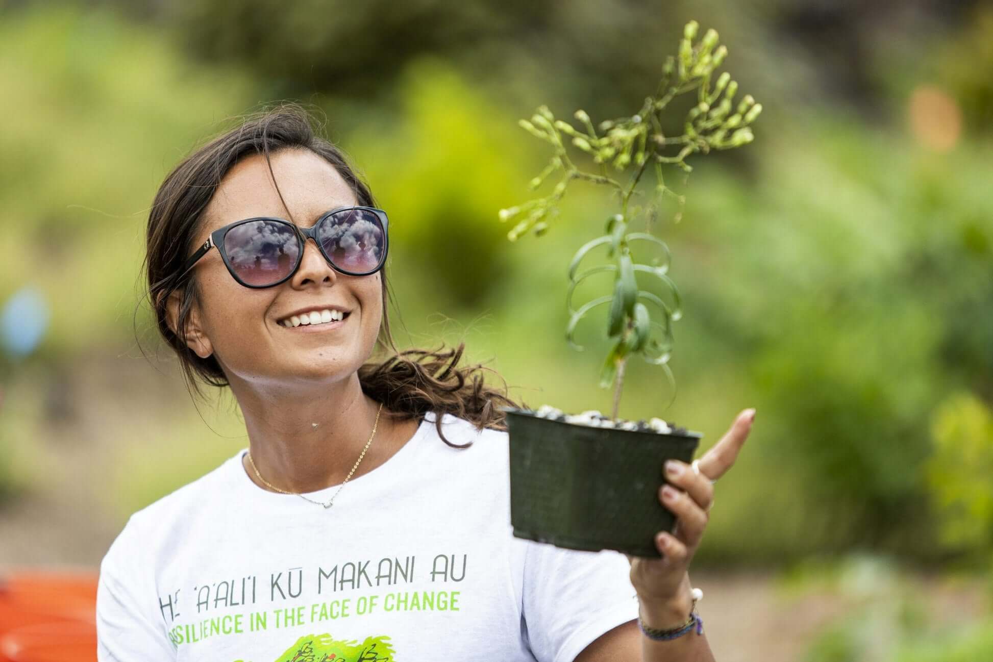 Teen volunteer in Hawaii smiles while holding a native plant, participating in environmental stewardship activities.
