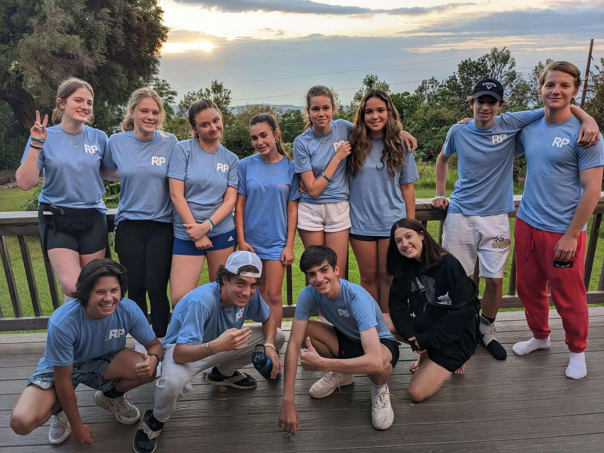 Group of high school teens in blue shirts smiling outdoors during summer service project in Hawaii.