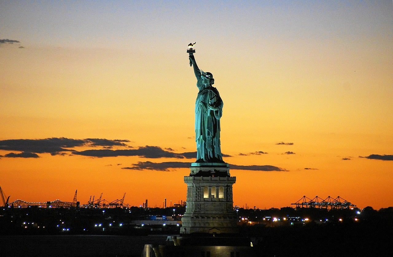 Statue of Liberty silhouetted against a vibrant sunset sky, symbolizing freedom and hope in New York Harbor.