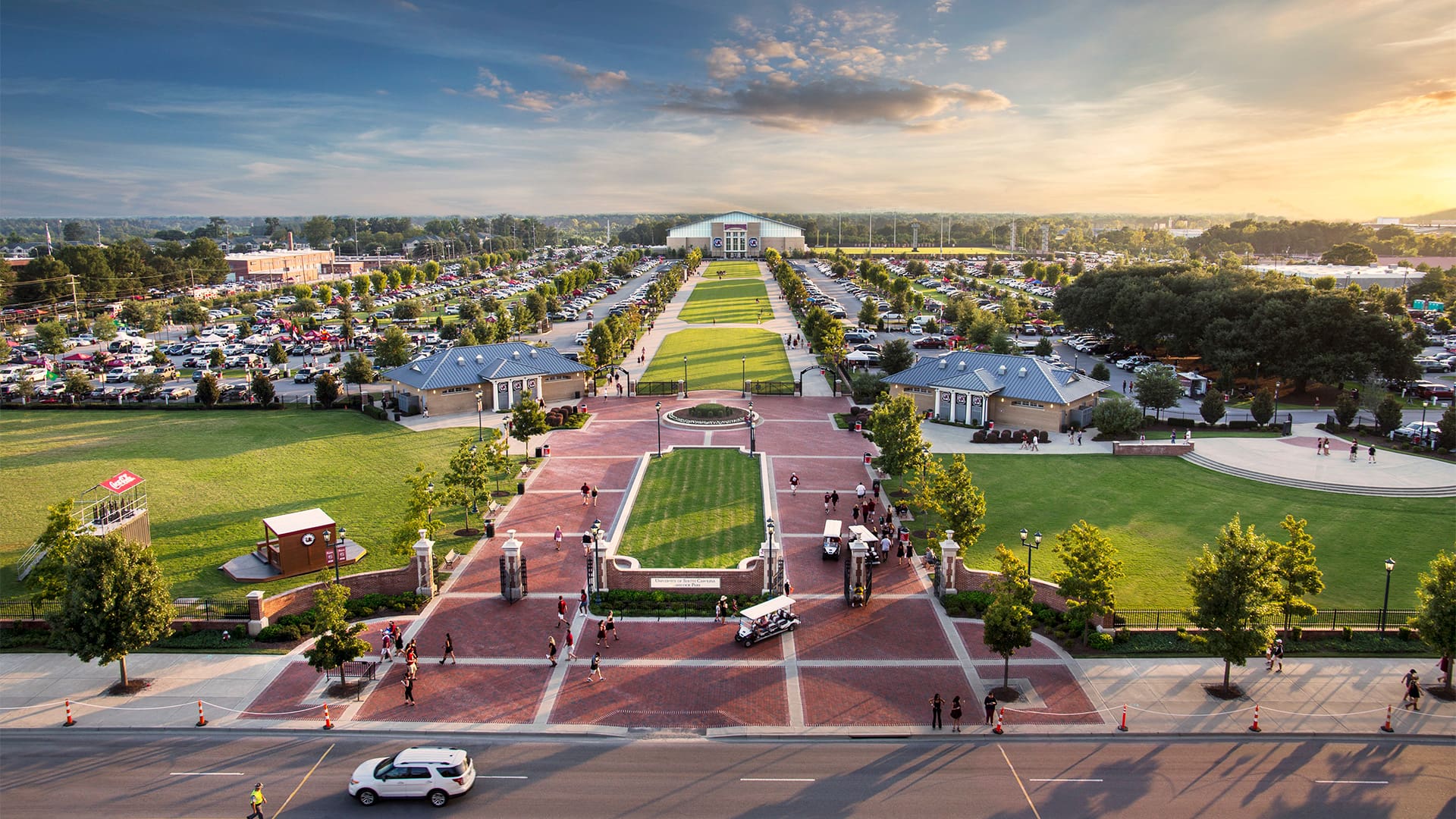 Aerial view of a large park with pathways, parking areas, and people enjoying the summer in a vibrant outdoor setting.