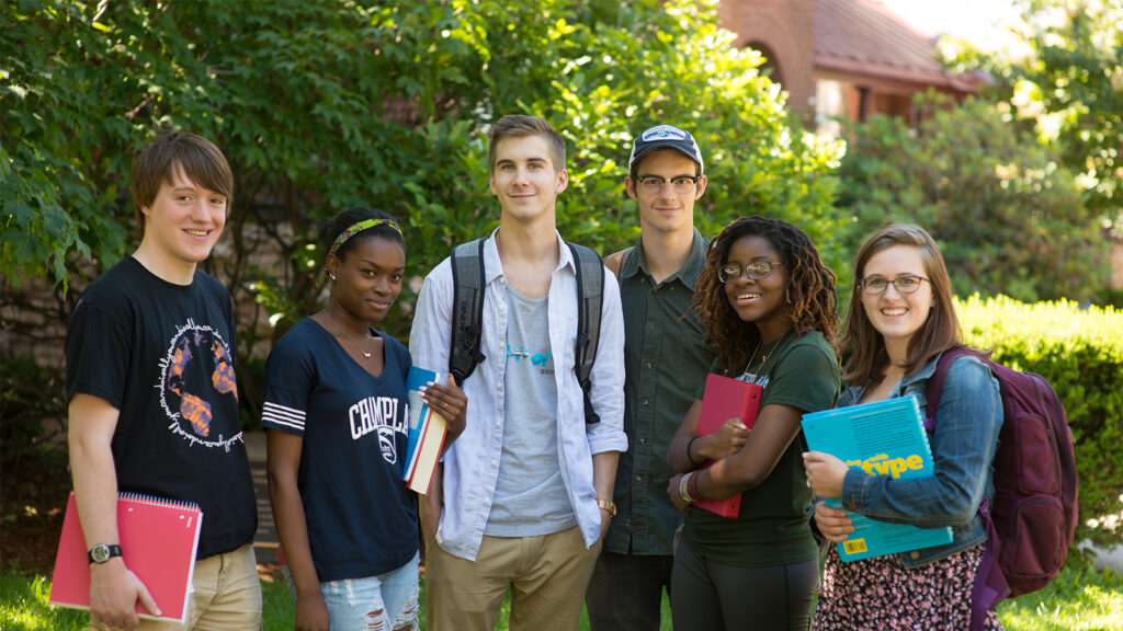 Group of diverse high school and college students standing together outdoors, smiling and holding books in summer.