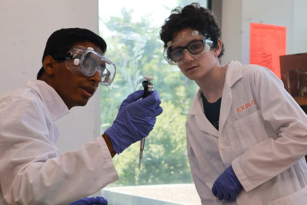 Two middle school students in lab coats engaging in a science experiment during a summer program at EXPLO.