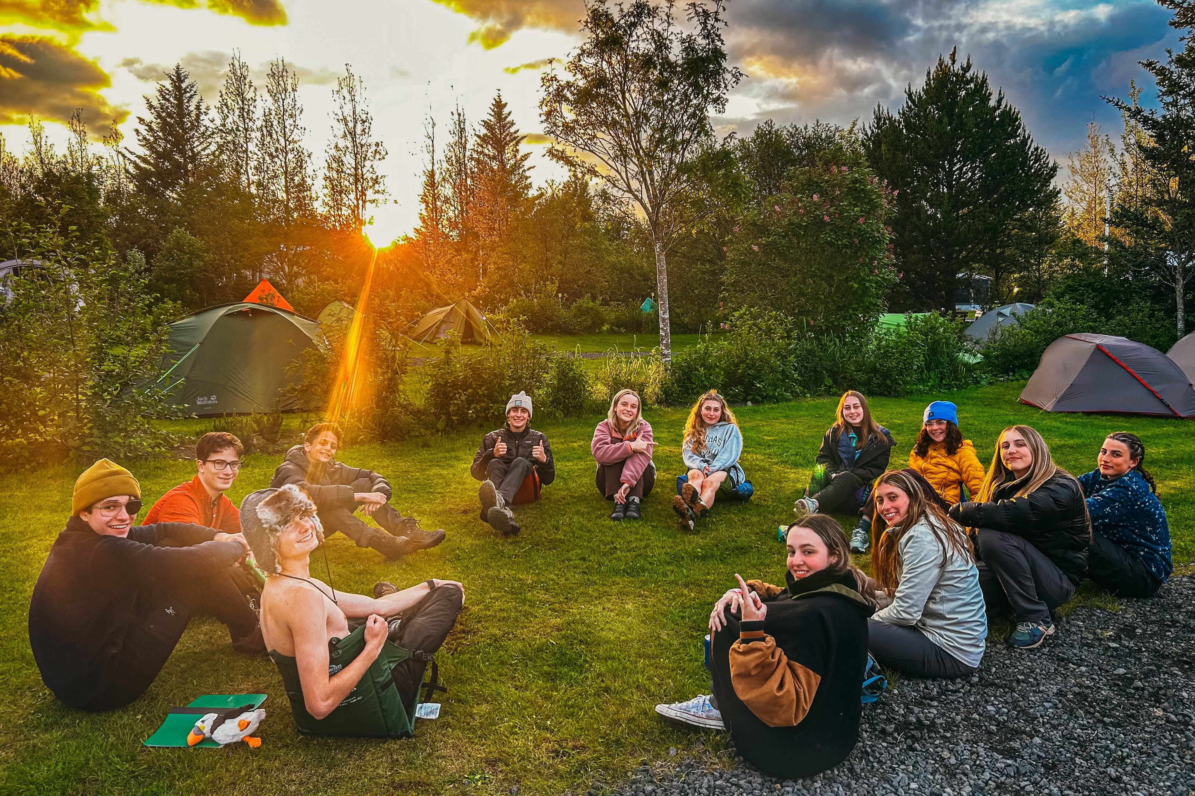 Group of high school students enjoying a summer camping experience in Iceland, surrounded by tents and nature at sunset.
