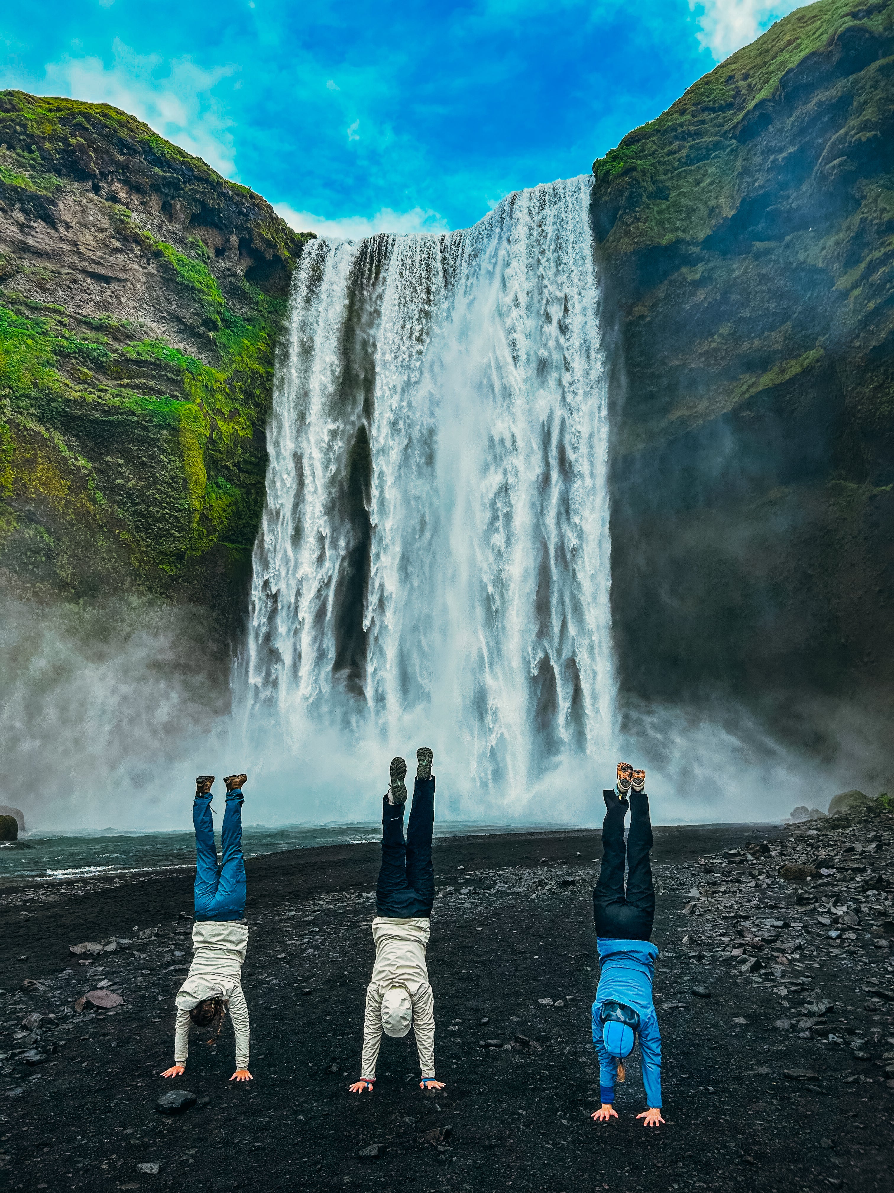 Three high school students doing handstands in front of a waterfall in Iceland, enjoying a summer adventure.