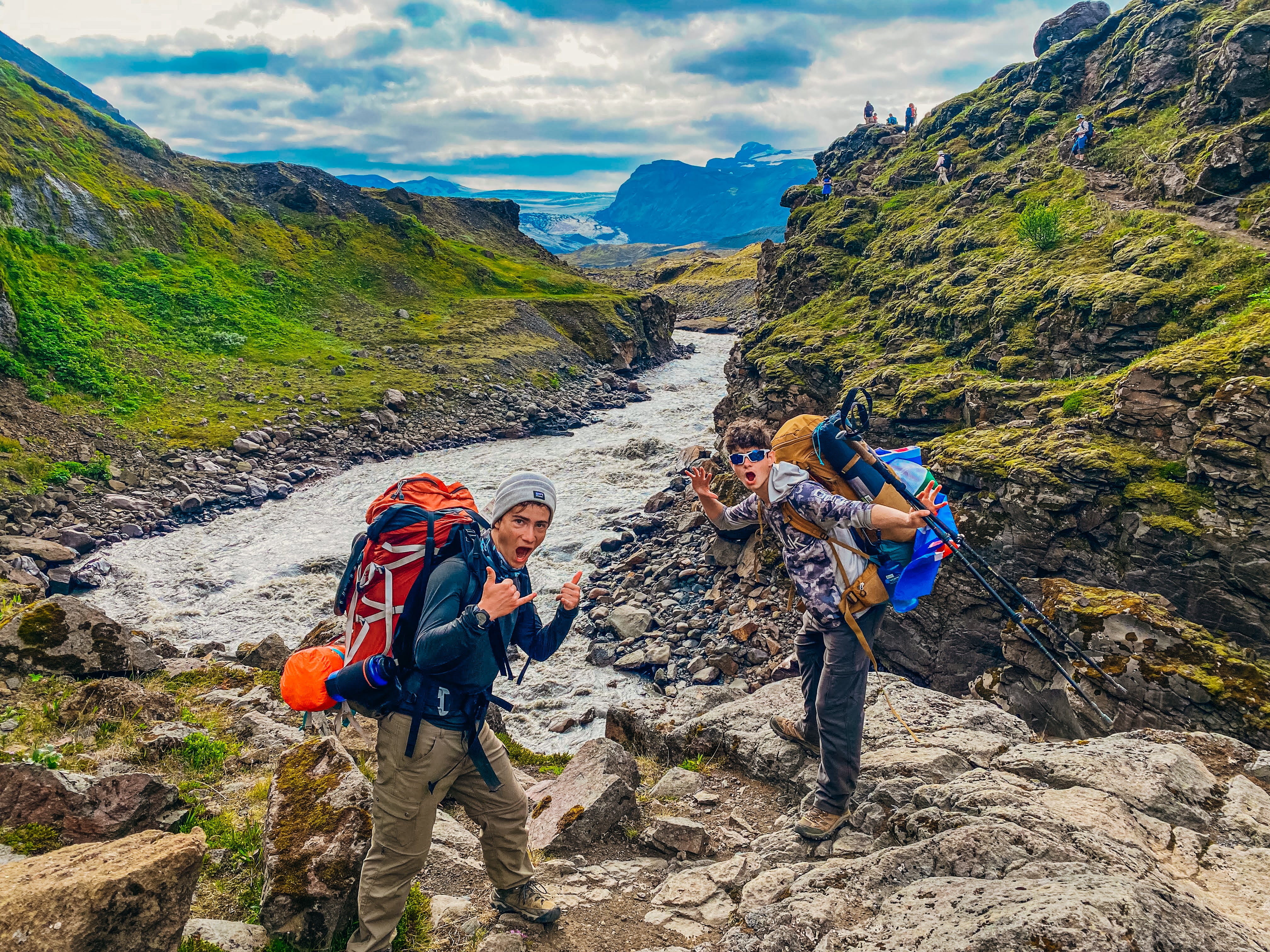 Two high school students enjoying summer hiking in Iceland's highlands with backpacks and a river in the background.