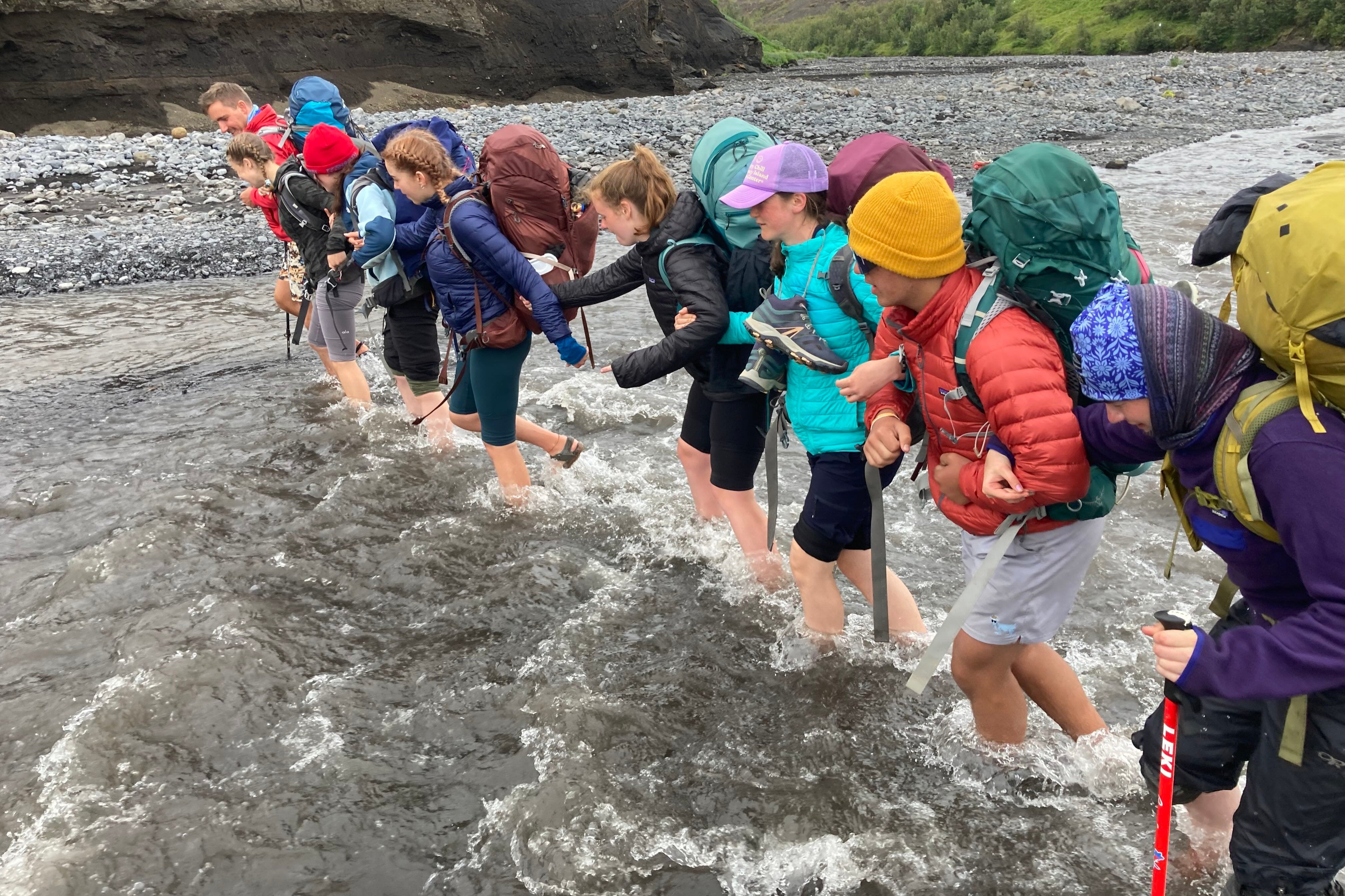 High school students crossing a river during a summer hiking program in Iceland's scenic highlands.