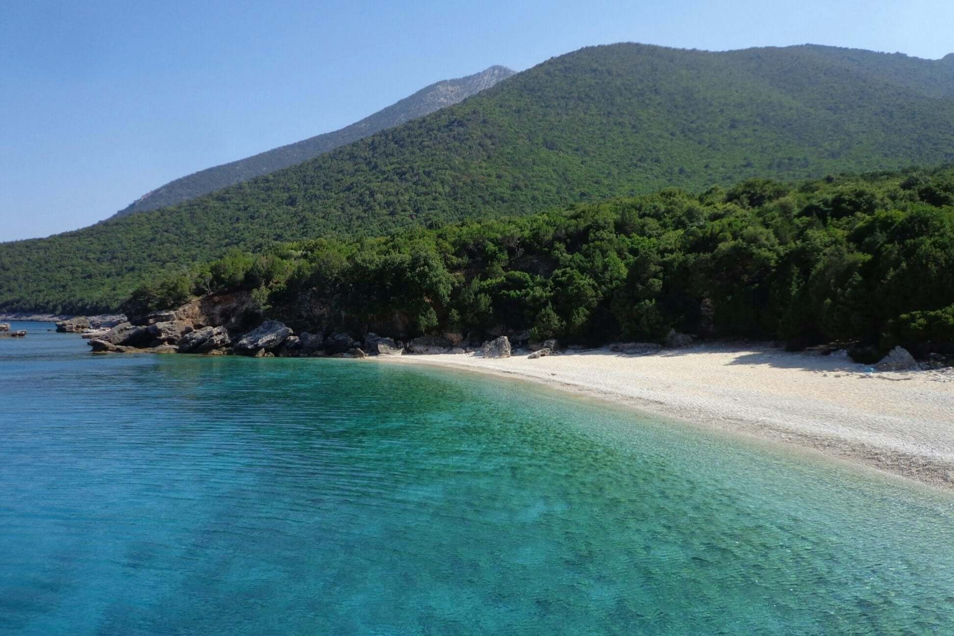 Serene beach view on a Greek Ionian Island, surrounded by lush greenery and clear turquoise waters, ideal for turtle conservation summer program.