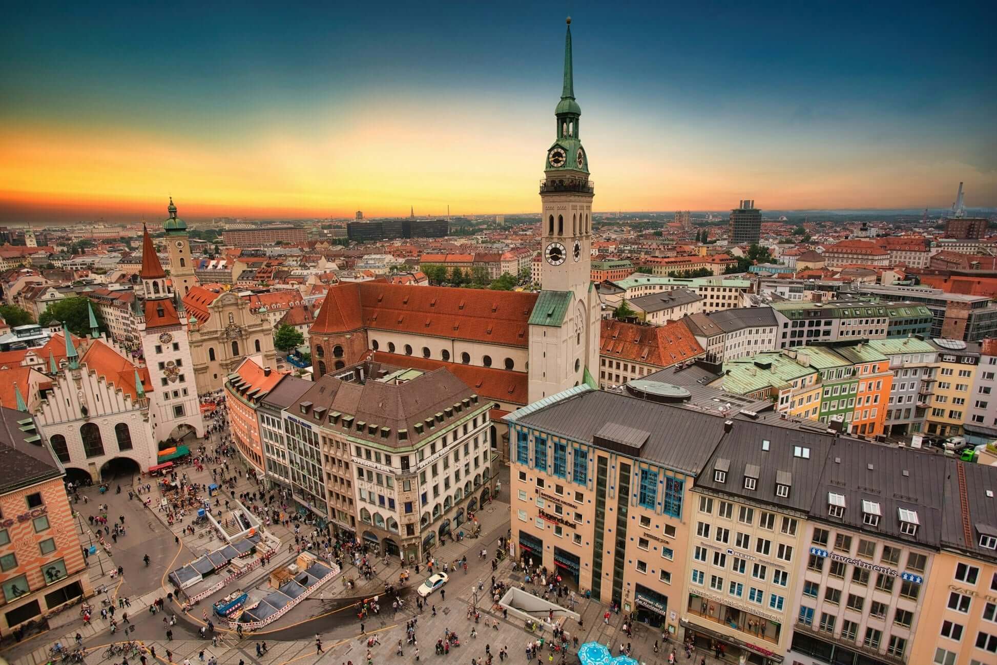 Aerial view of Munich's cityscape at sunset, showcasing historic buildings and bustling streets below.
