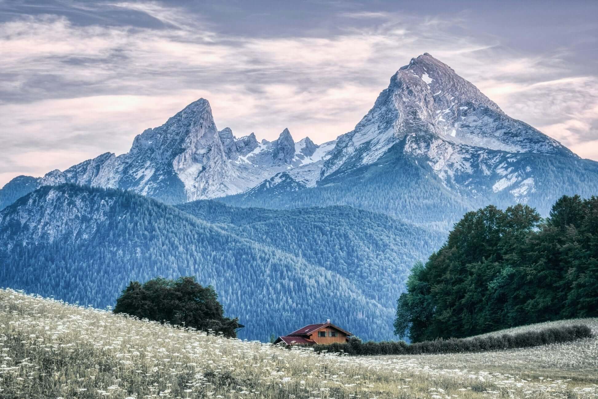 Scenic view of majestic mountains and a peaceful meadow with a house, showcasing natural beauty and tranquility.