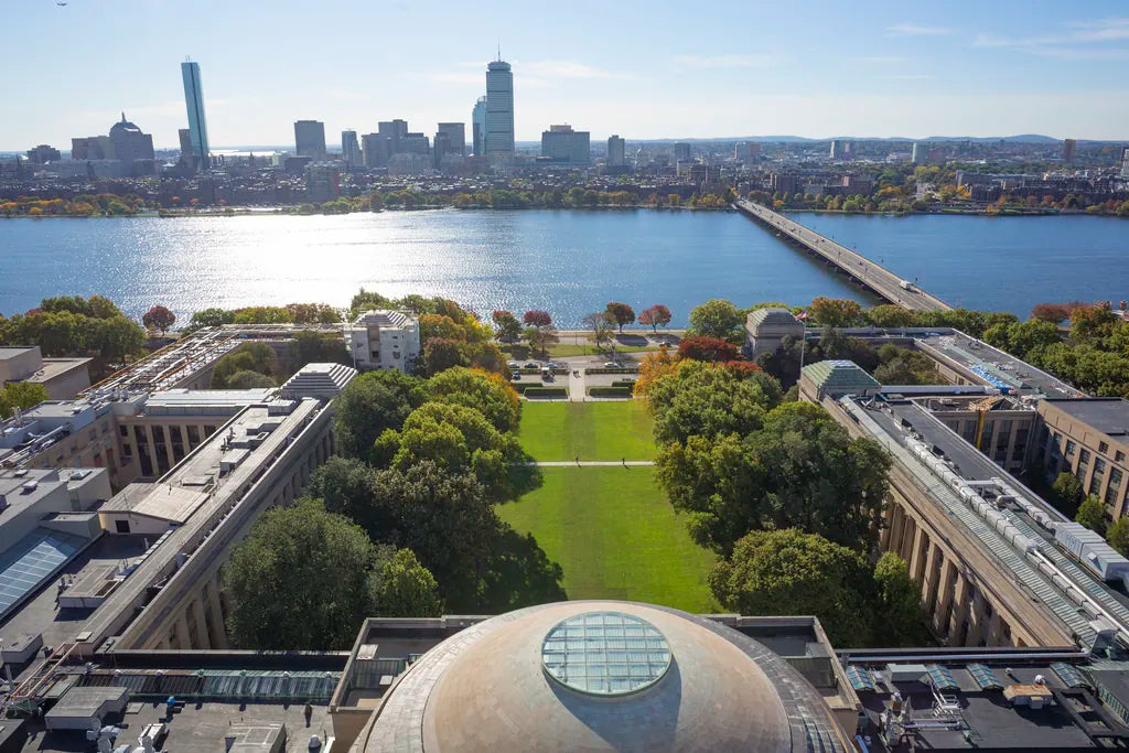 Aerial view of the Charles River, Boston skyline, and tree-lined campus, showcasing vibrant autumn colors and iconic architecture.