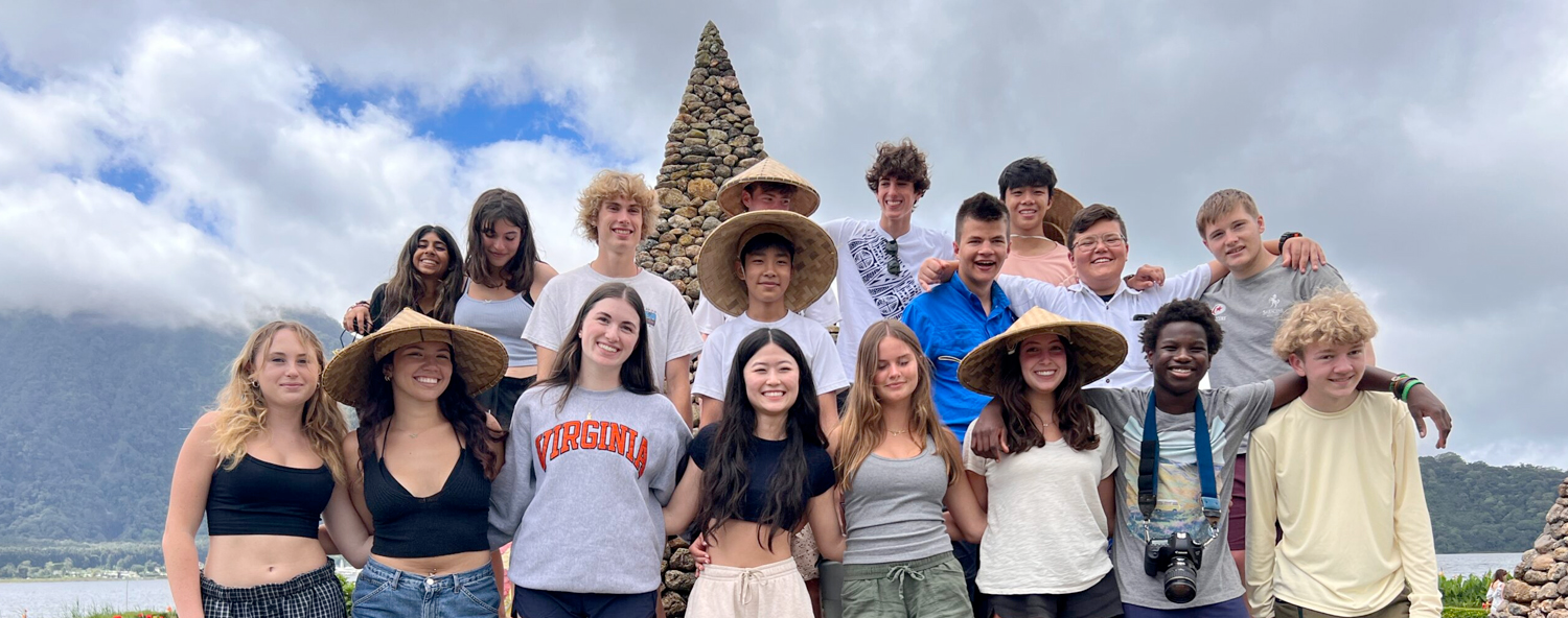 Group of high school students participating in a summer camp program outdoors with straw hats and scenic background.