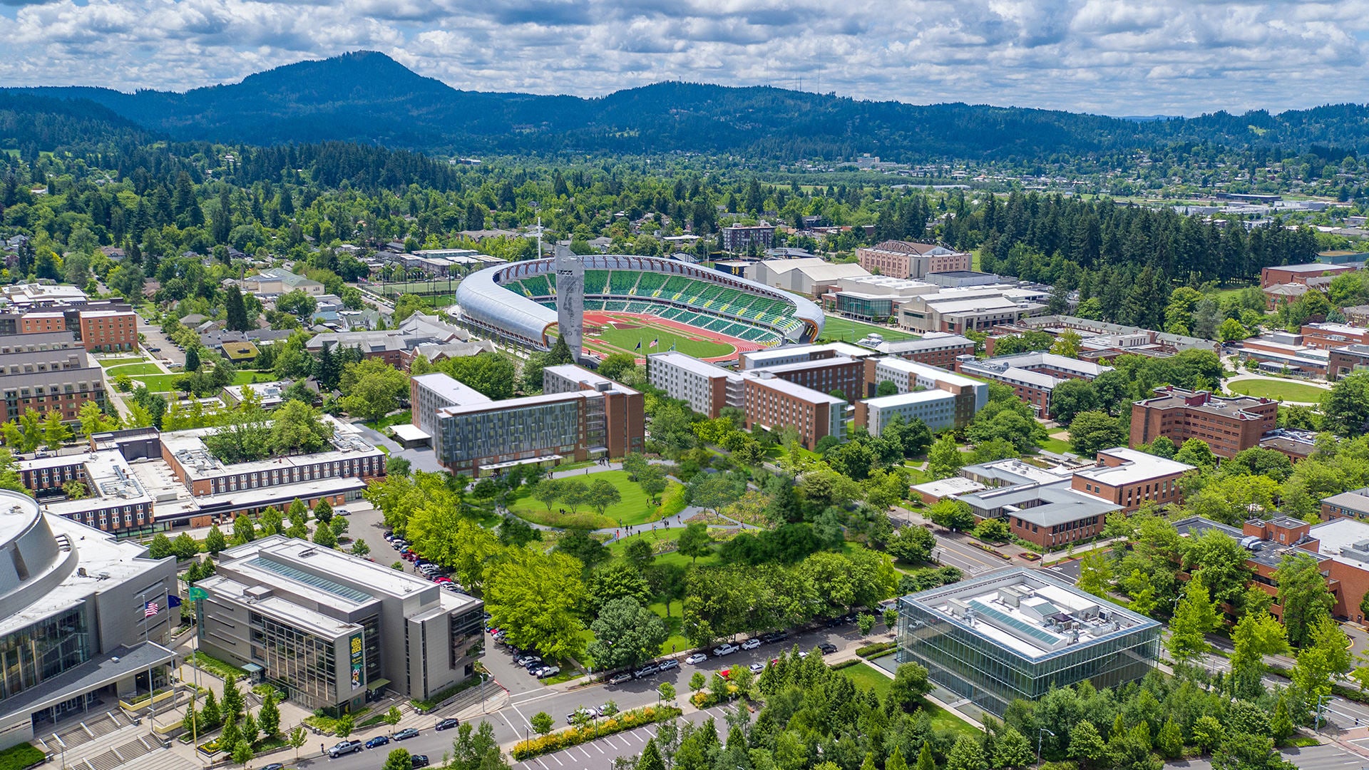 Aerial view of a college campus featuring green fields, residential buildings, and a large stadium surrounded by trees.