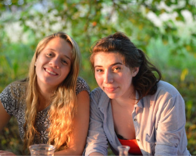 Two smiling girls enjoying a summer camp experience outdoors at sunset.