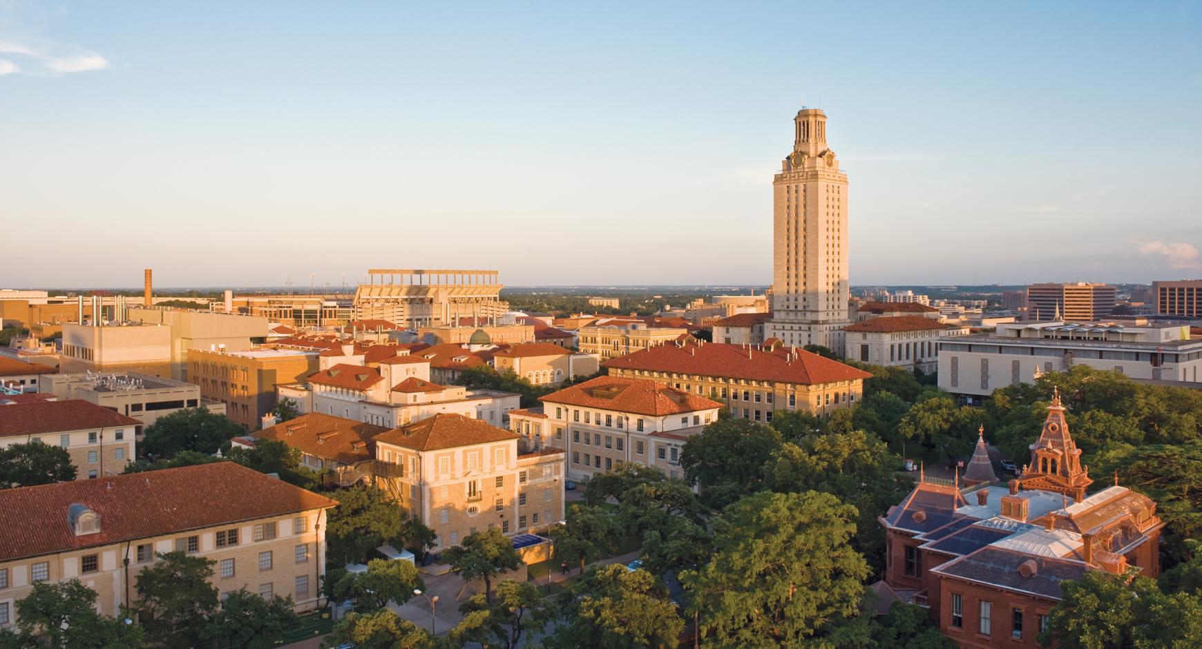 Aerial view of a campus with historic buildings and a tall tower, showcasing a vibrant urban landscape at sunset.