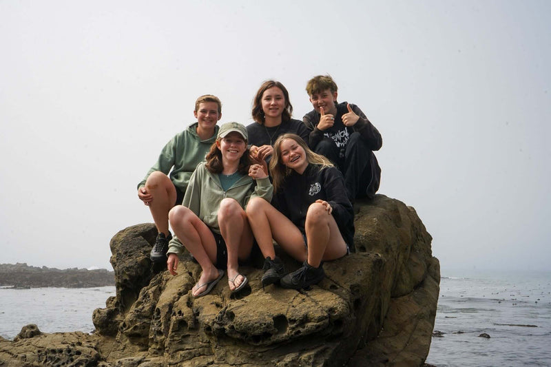 Group of kids enjoying time at Camp Ocean Pines, California, on a rocky beach during summer camp.