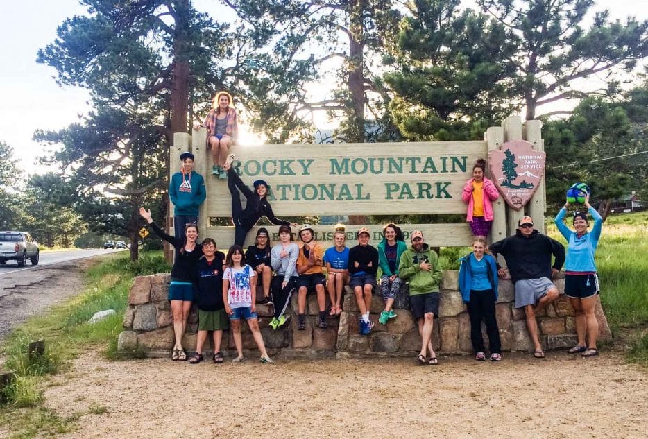 Group of teens celebrating at the Rocky Mountain National Park entrance during a summer adventure program.