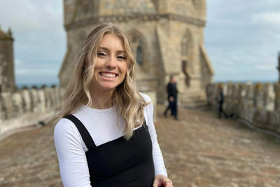 Young woman smiling at a historic tower, enjoying her summer travels in Portugal. Perfect for teen travel programs.